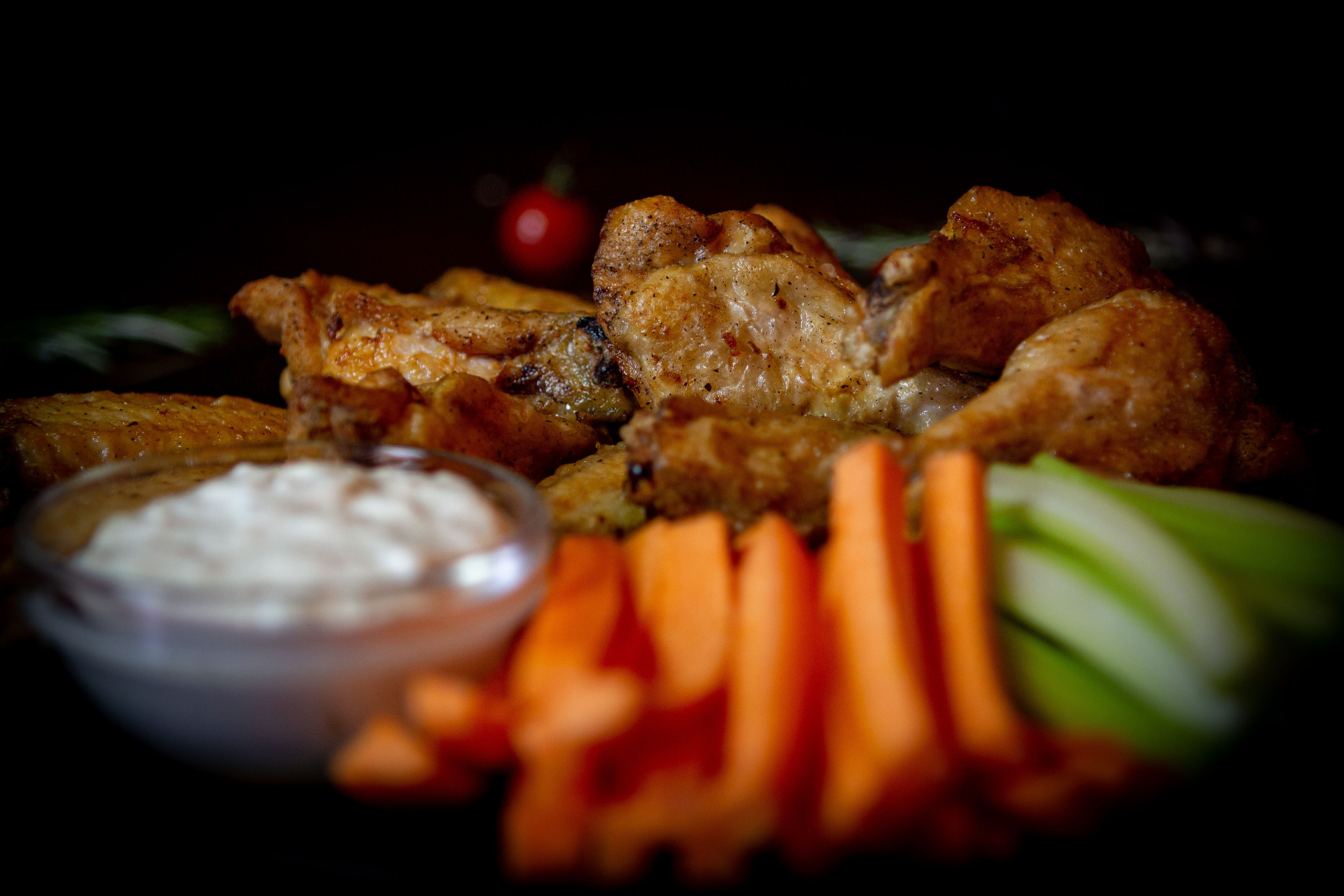 Куриные крылья, приготовленные на гриле, с овощным ассорти и соусом терияки, представлены на керамической тарелке