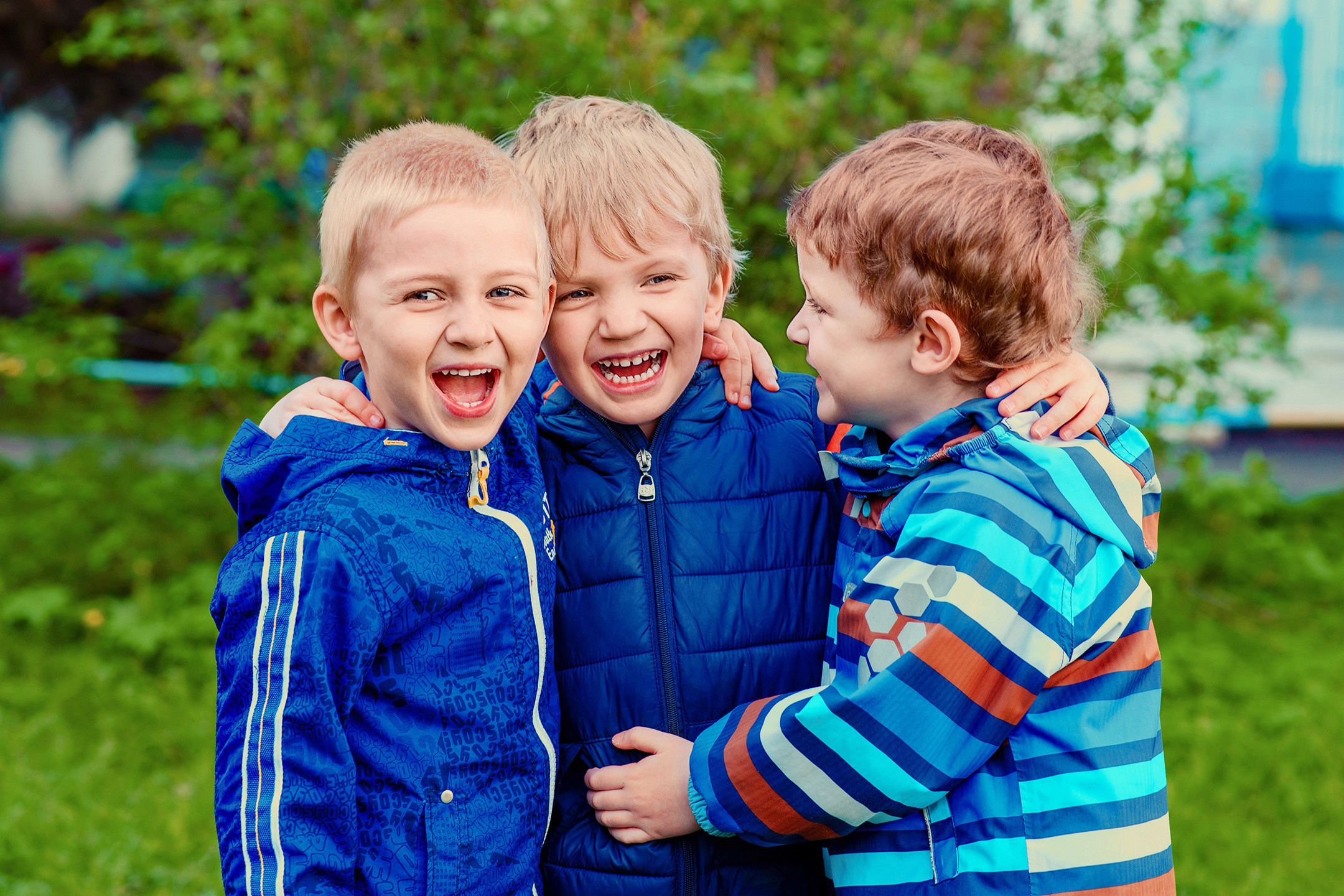 Трое смеющихся мальчиков на весенней прогулке в детском саду.
