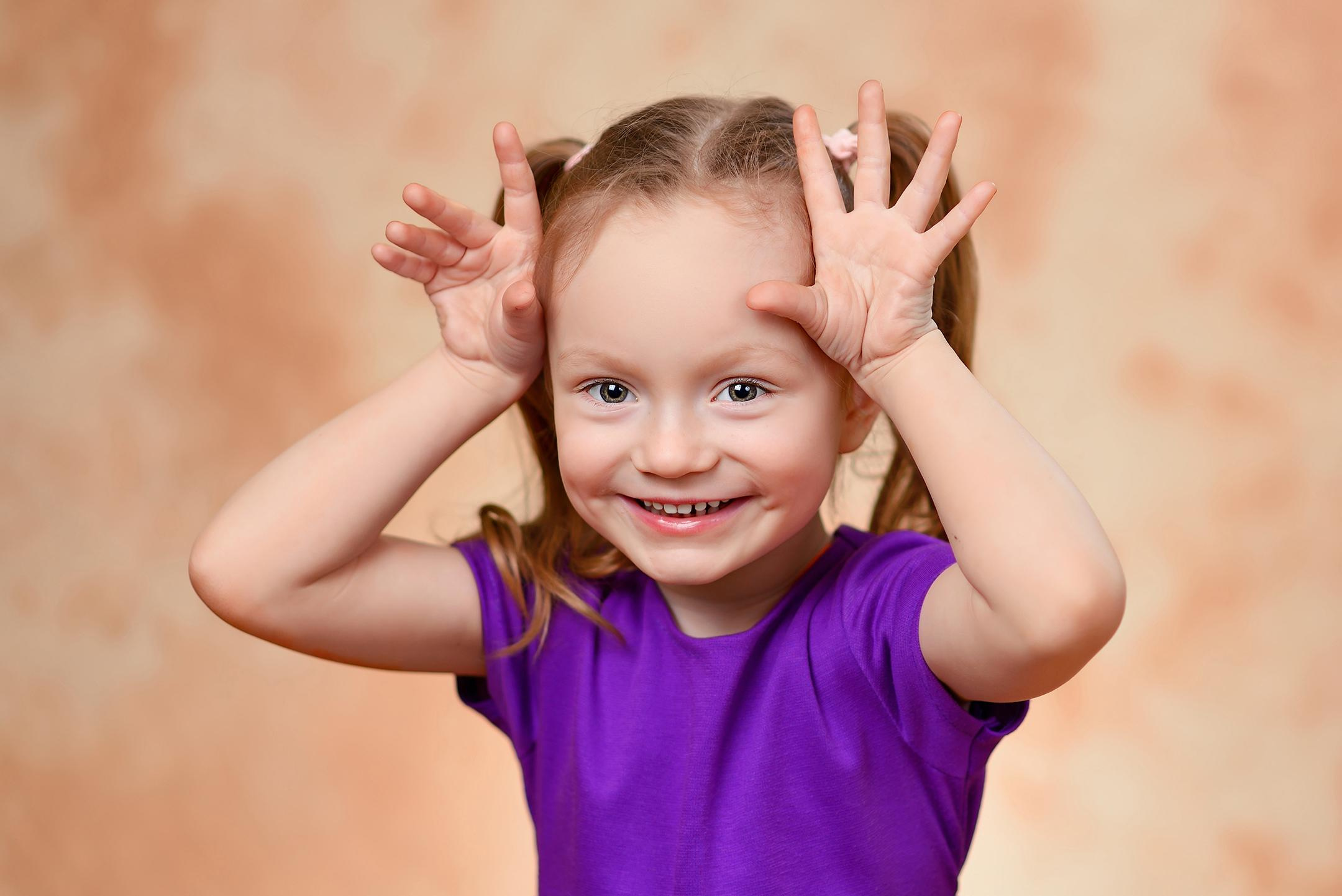 Игровой эмоциональный портрет улыбающейся девочки в детском саду на студийном фоне.