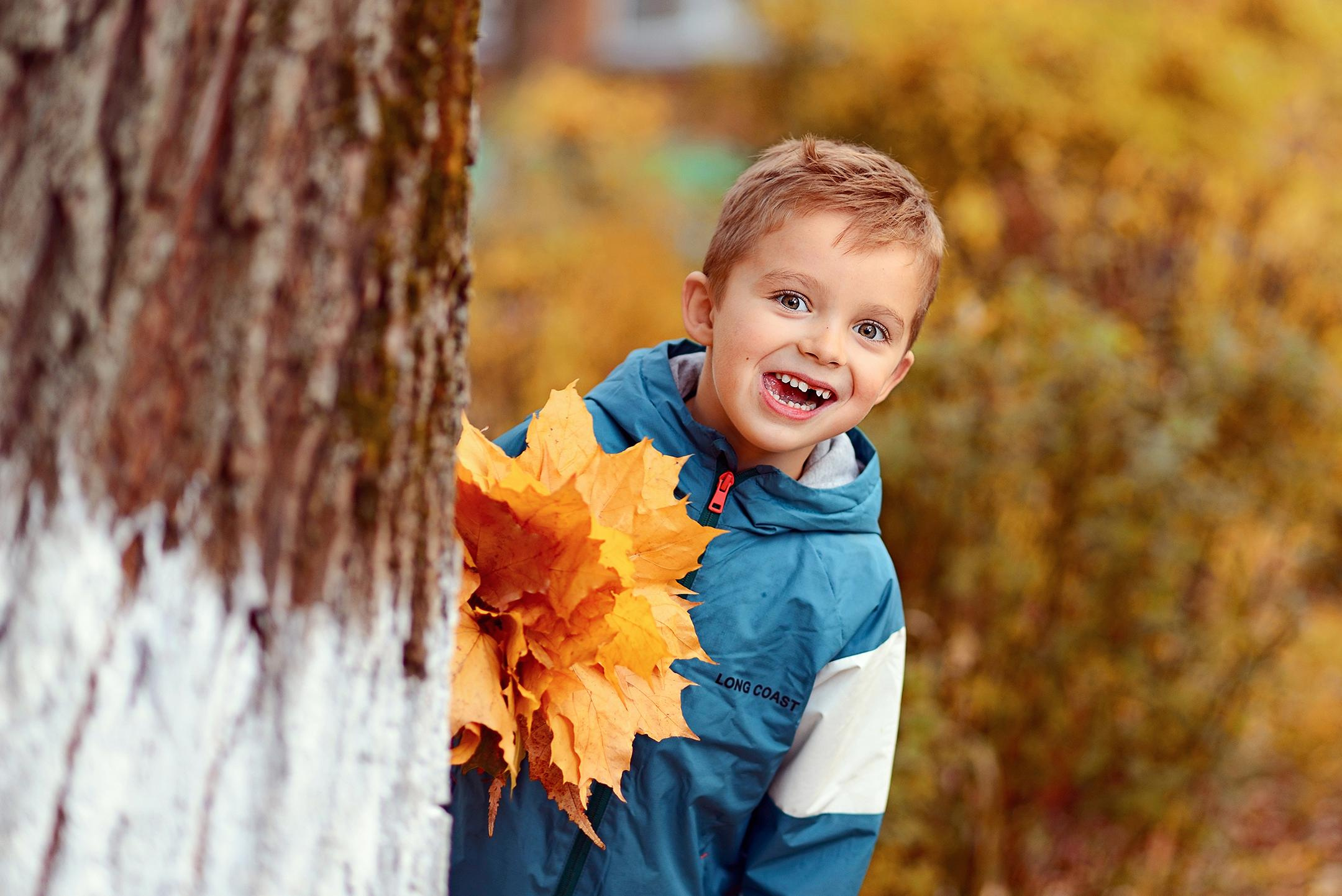 Мальчик с осенним букетом выглядывает из-за дерева.