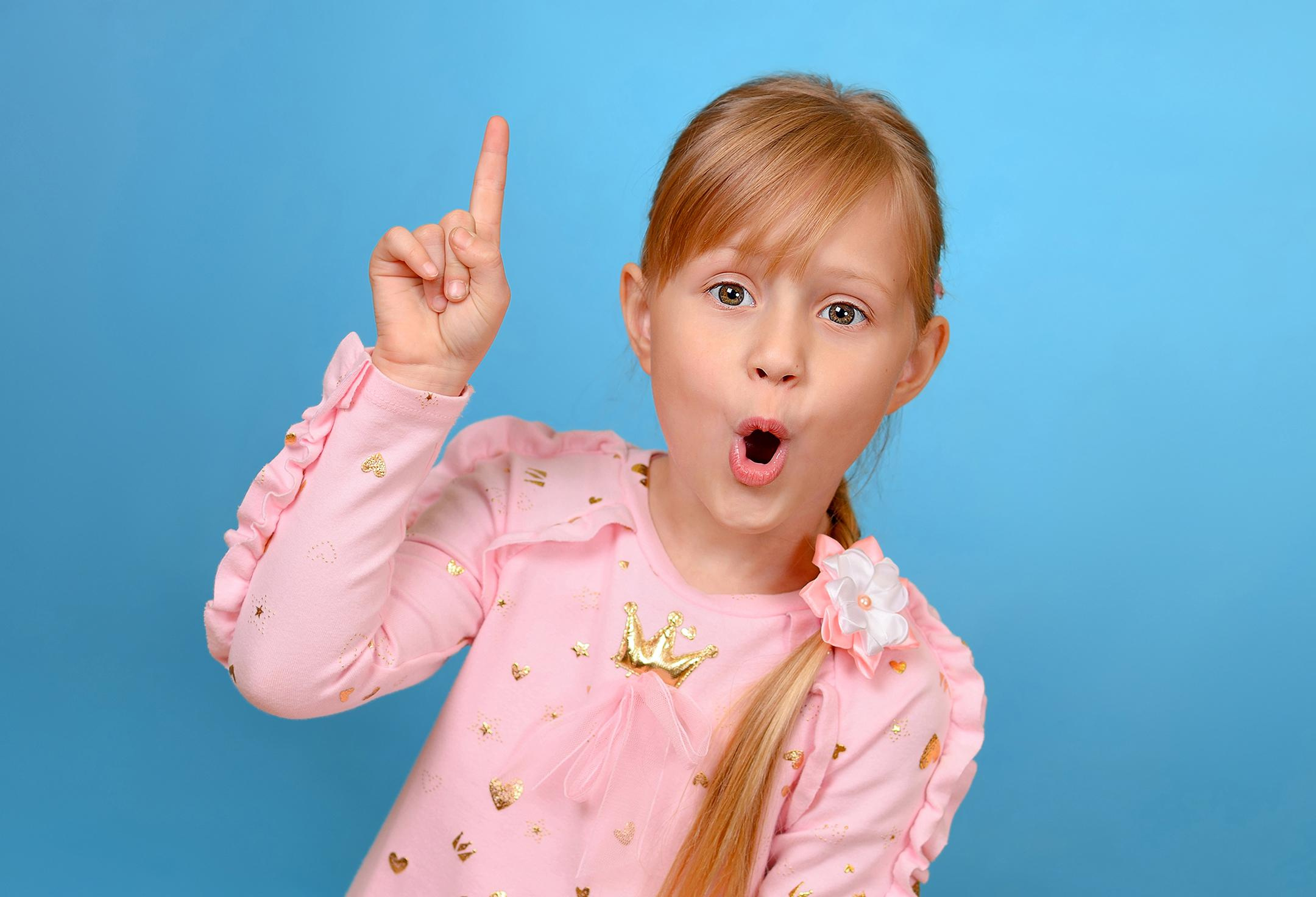 Игровой эмоциональный портрет удивлённой девочки, поднявшей палец вверх, потому что ей в голову пришла идея.