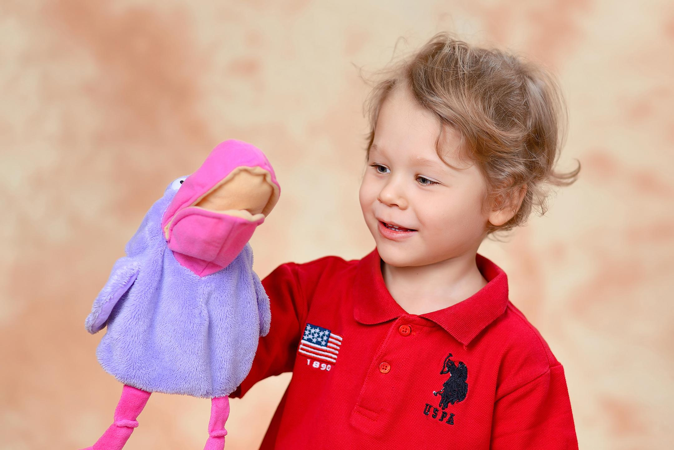 Эмоциональный портрет улыбающегося мальчика, который играет с игрушечной вороной.