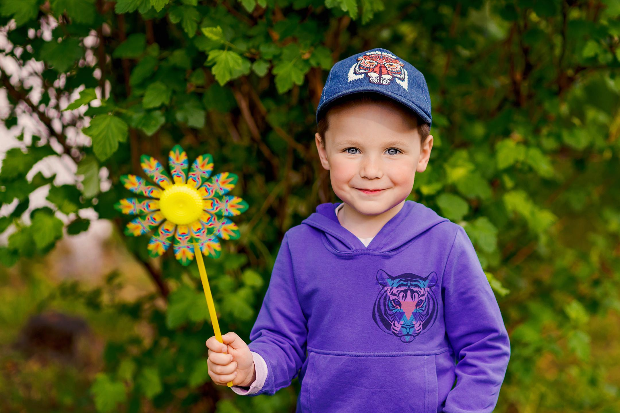 Мальчик держит флюгер в виде цветка на весенней прогулке в детском саду.