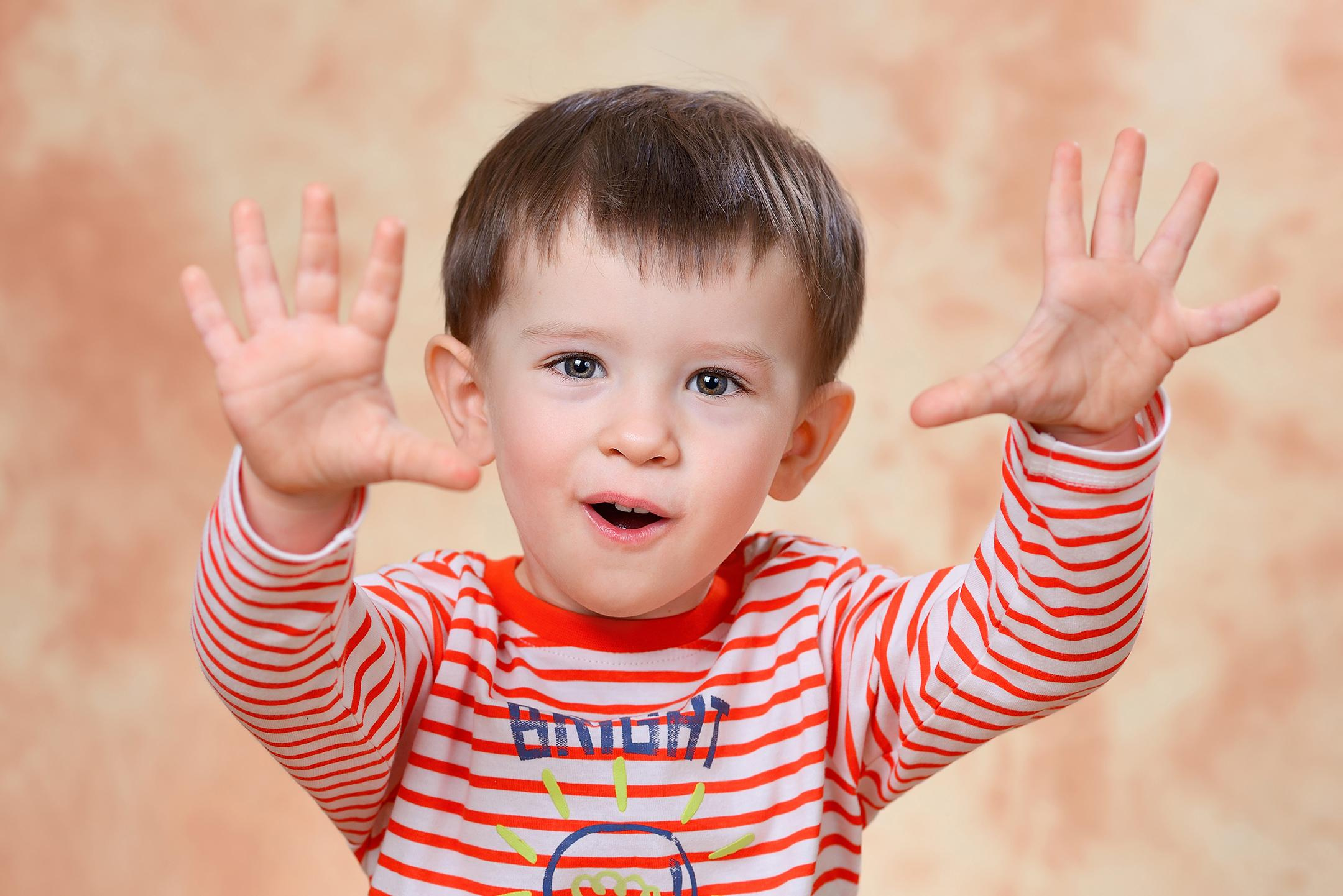 Игровой эмоциональный портрет мальчика, выставившего вперёд руки, чтобы напугать фотографа.