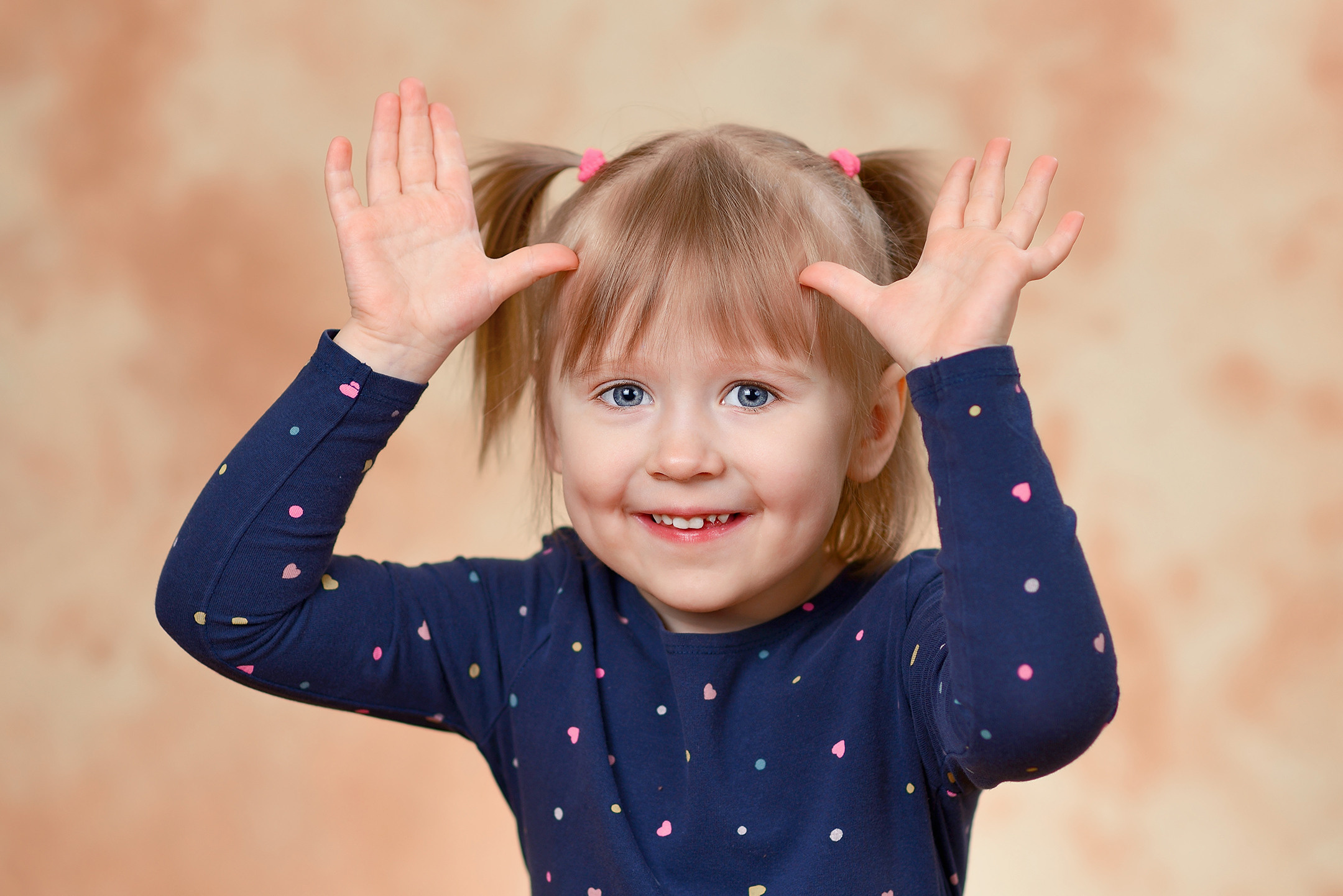 Игровой эмоциональный портрет улыбающейся девочки в детском саду на студийном фоне.