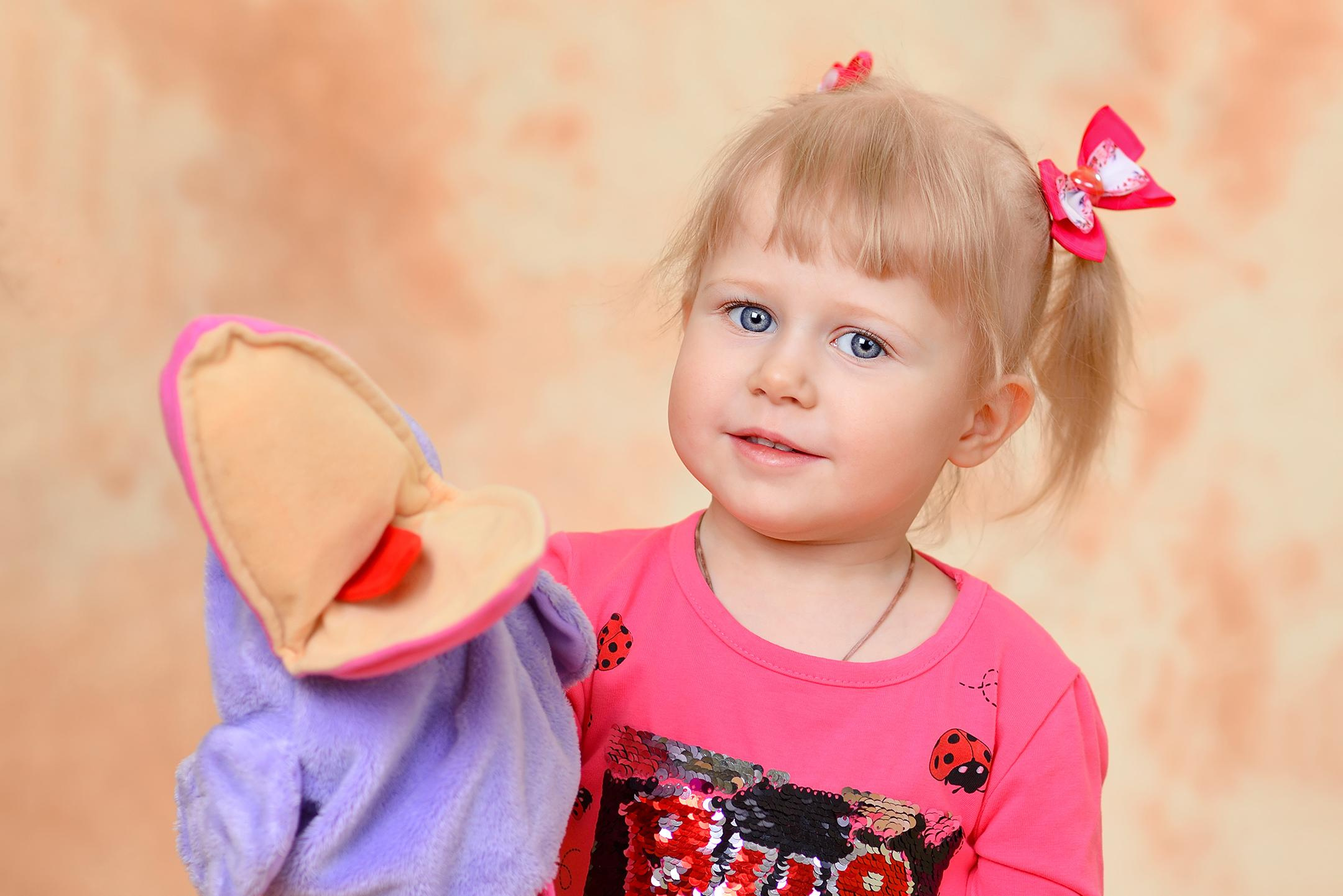 Портрет девочки на бежевом фоне, играющей с вороной, надетой на руку.