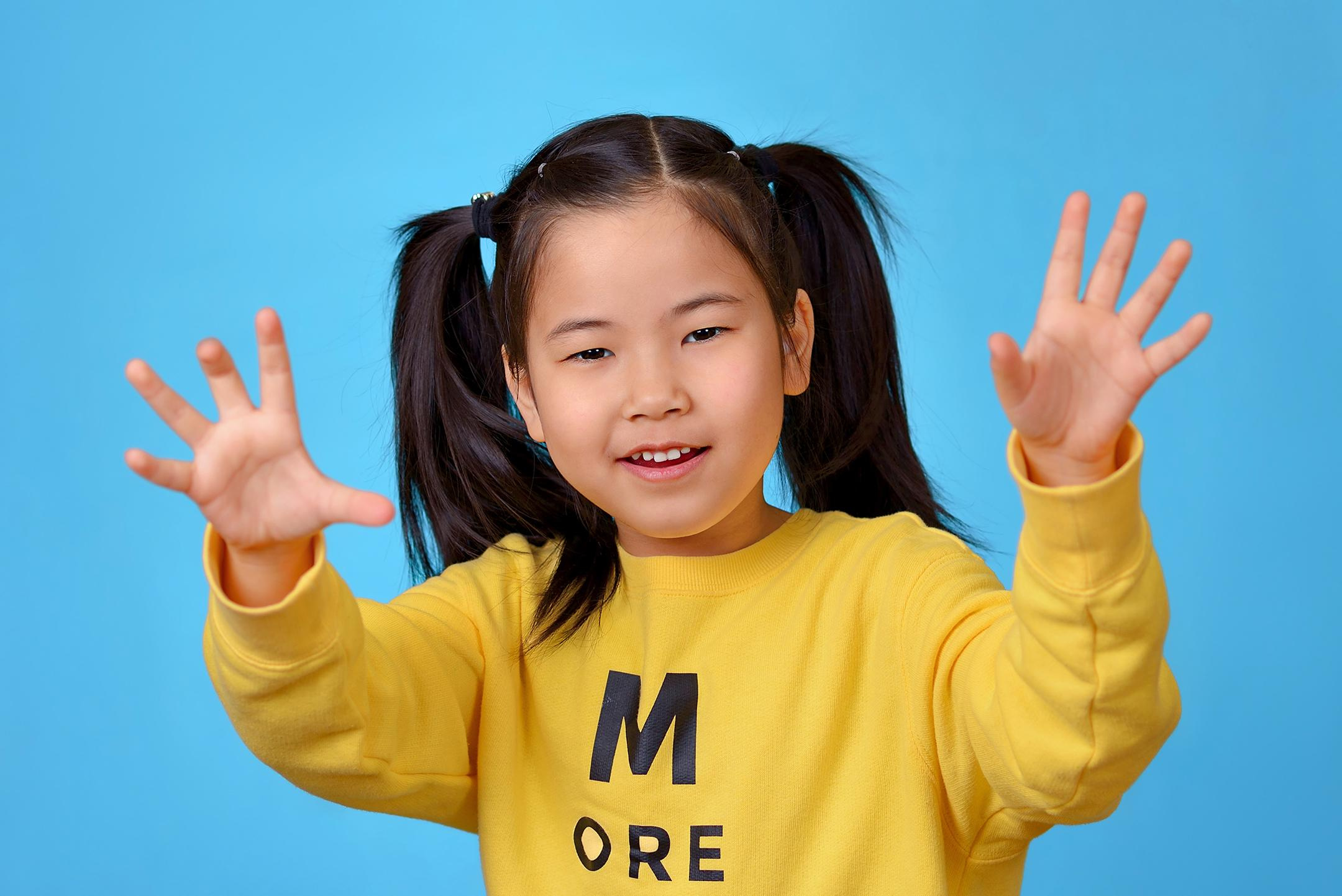 Игровой портрет девочки на голубом фоне, выставившей вперёд руки, чтобы напугать фотографа.