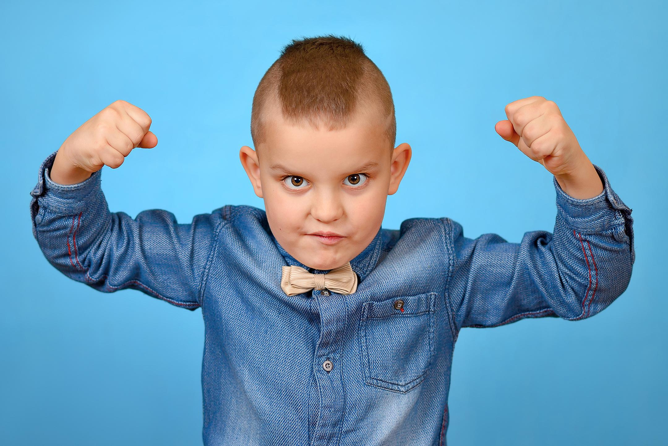 Мальчик смотрит исподлобья, сжав руки в кулаки, показывая, какой он сильный и грозный.