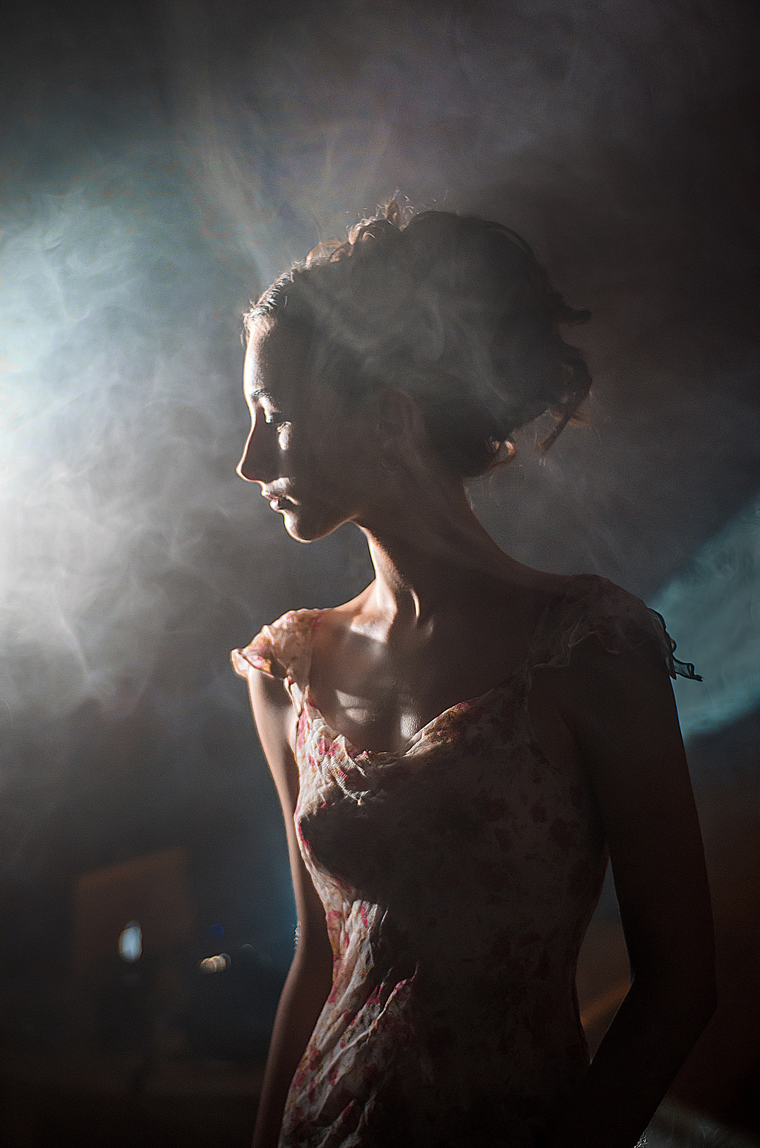 девушка стоит в профиль в лучах света, красивая фотосессия с дым машиной