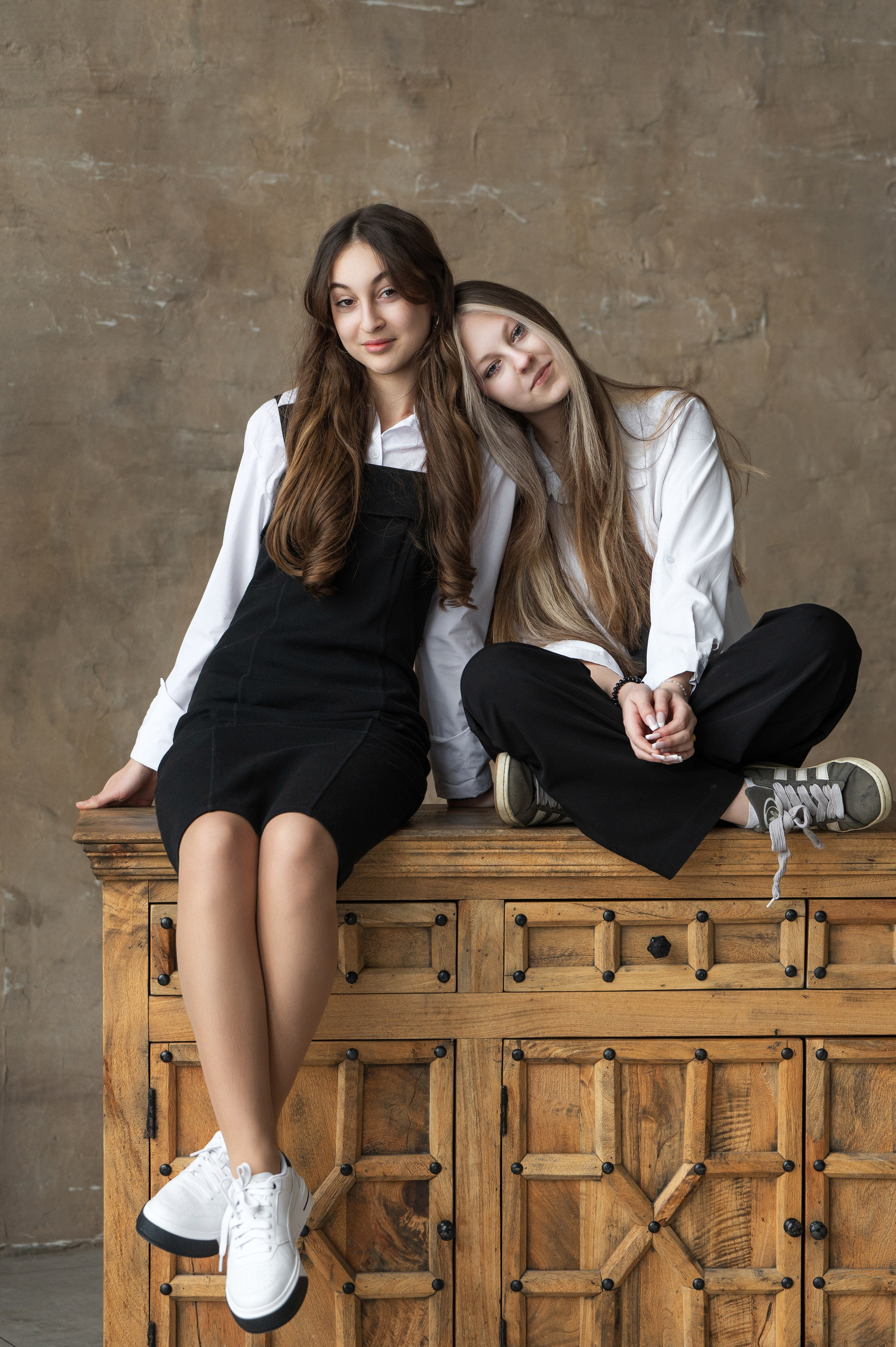 Две подруги сидят рядом на деревянной тумбе в парном кадре для школьного альбома.