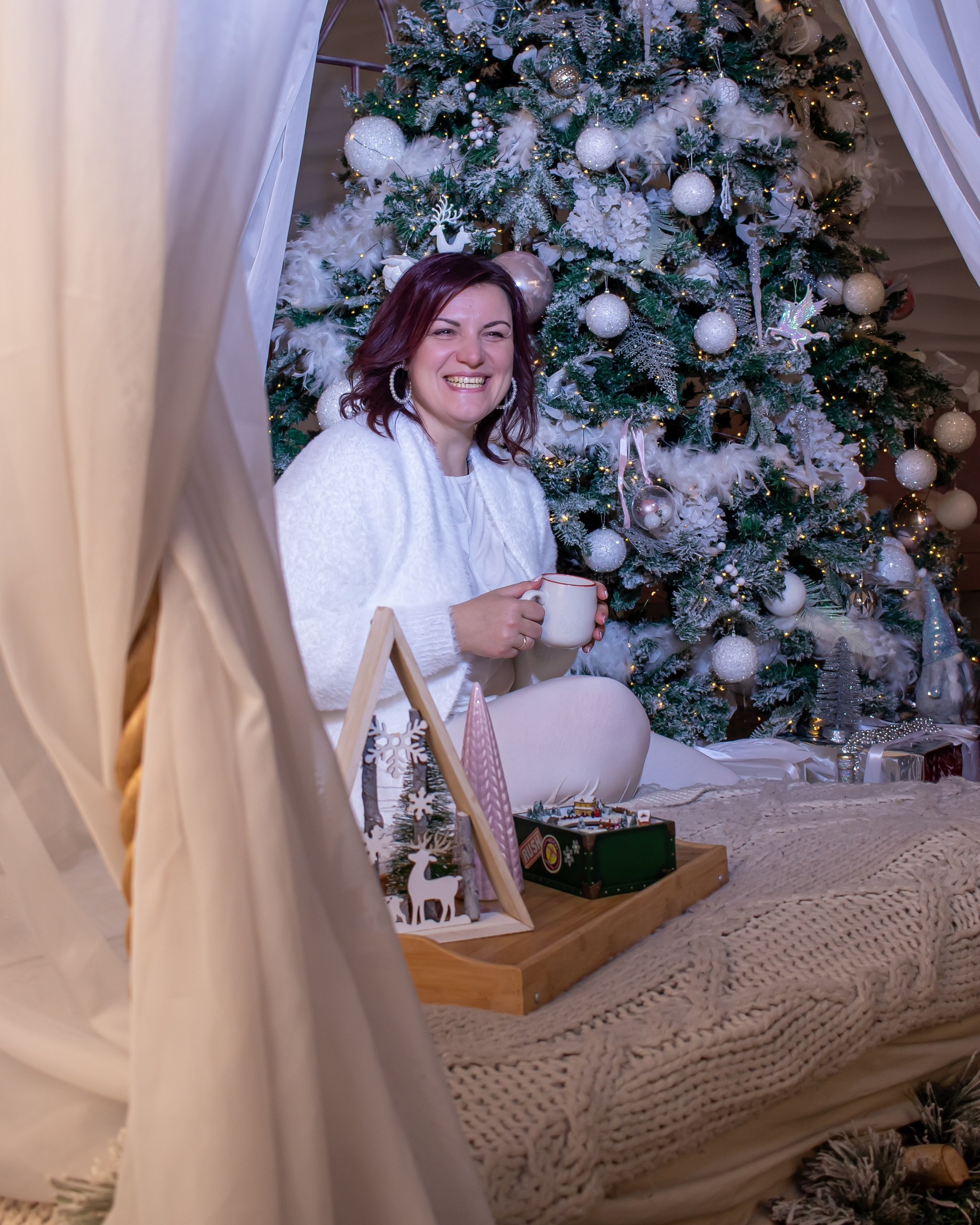 Женщина лежит на покрывале среди зимнего белого декора и мягкого света, рождественская фотосессия, фотограф Карасёва Елена