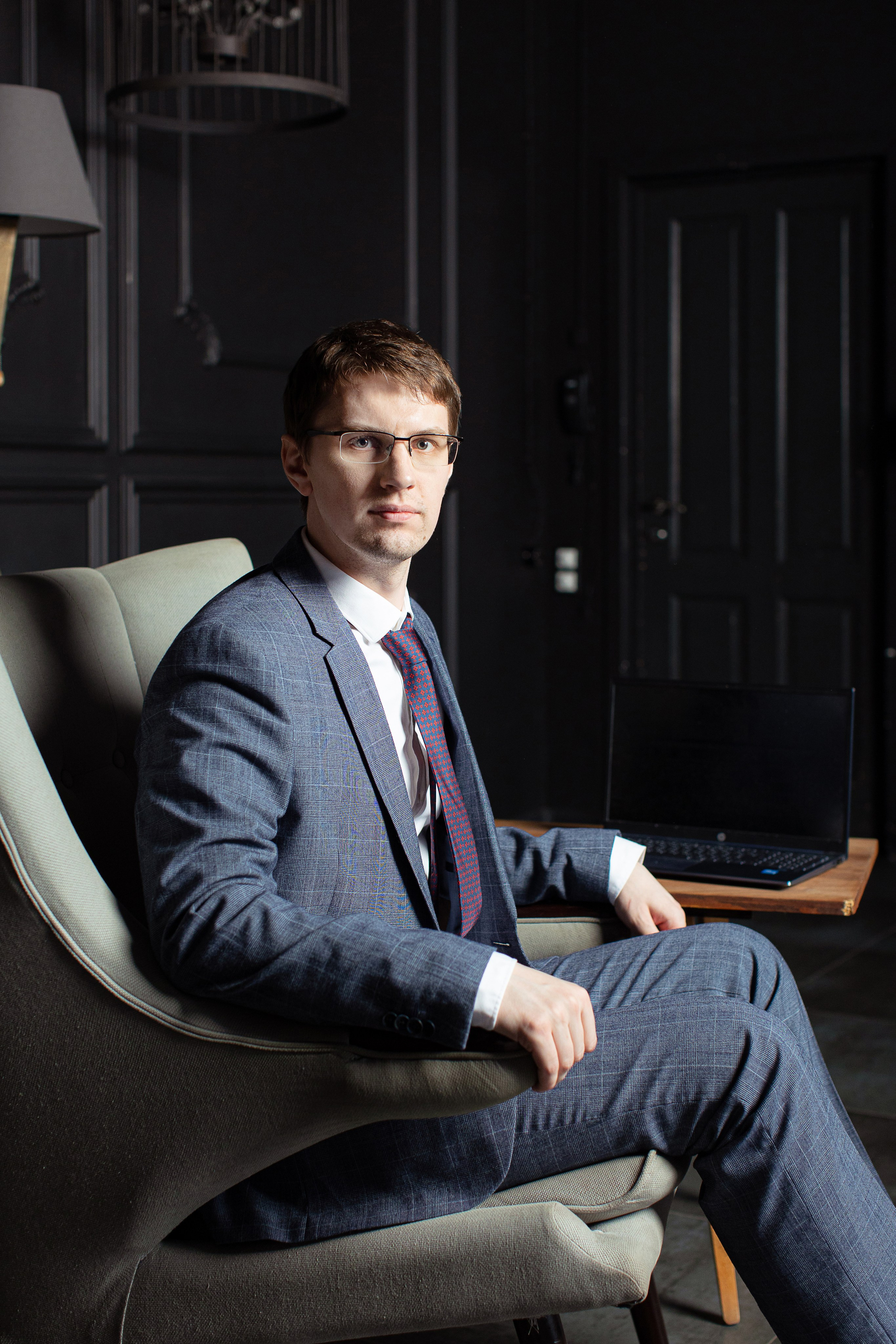 Мужчина в костюме с галстуком и в очках сидит в кресле