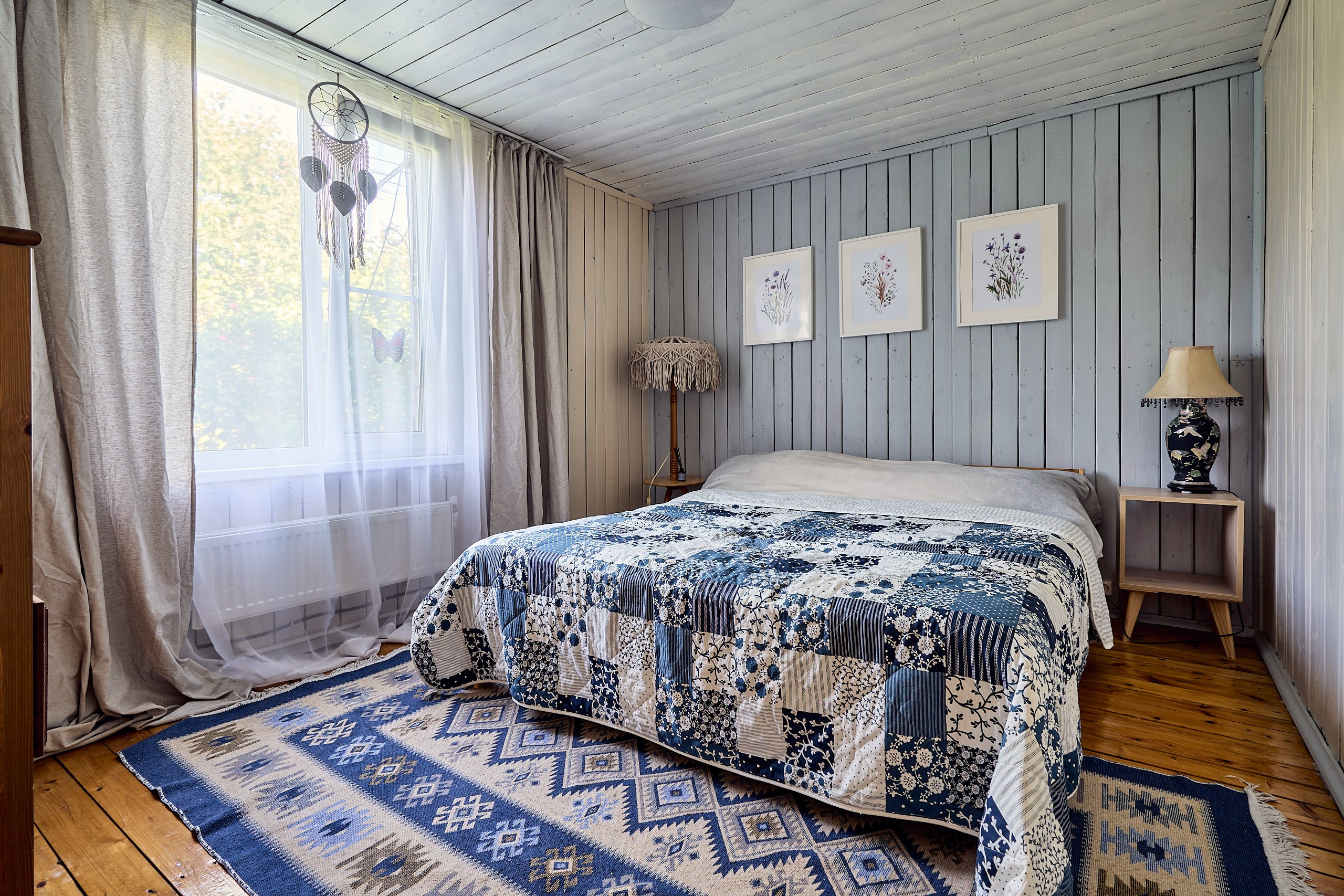 Интерьерная фотография в спальне в мезонине загородного дома, общий план с окном, двуспальной кроватью, прикроватным ковриком, светильниками и интерьерной живописью