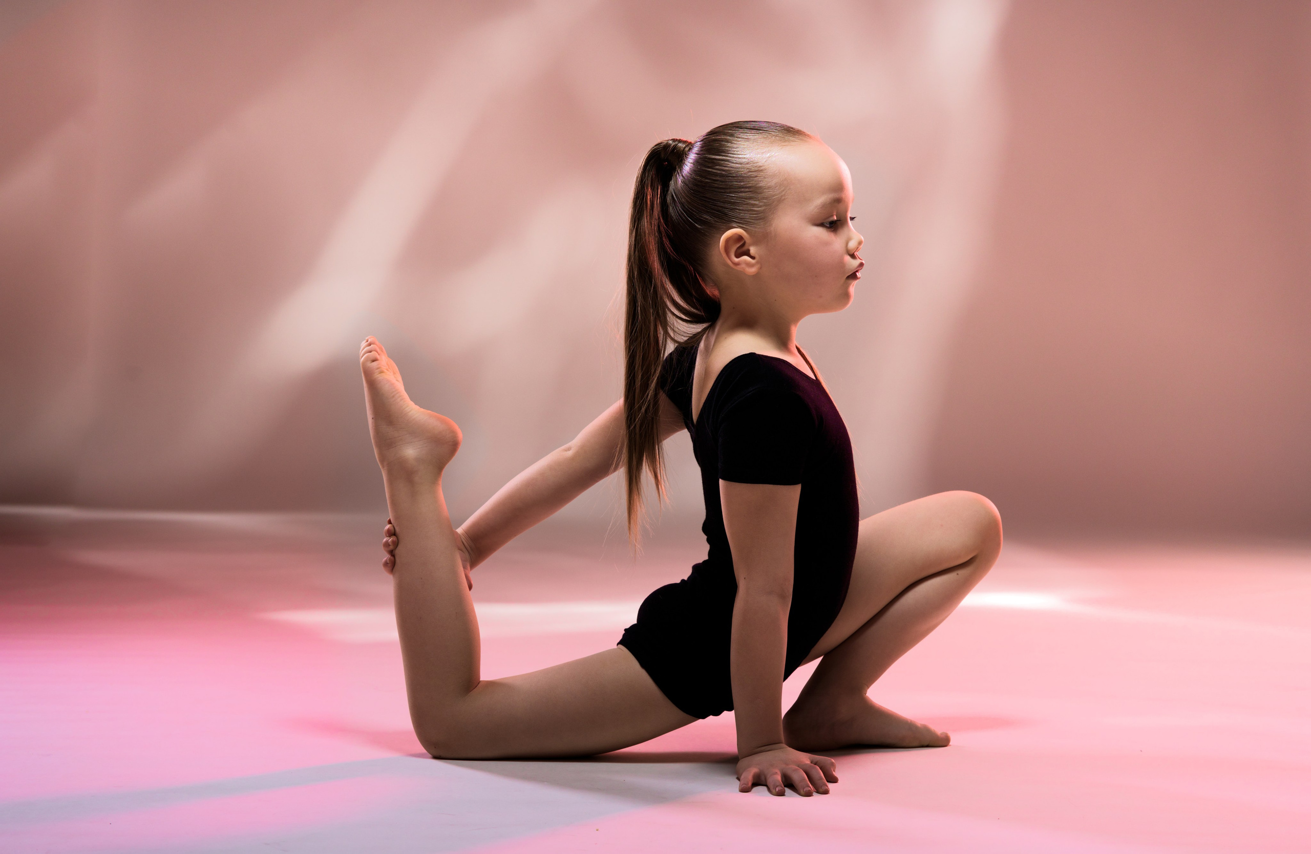 Портрет девочки-гимнастки в профиль во время тренировки. Эстетика детского спорта и грации, мягкие световые блики на фоне.