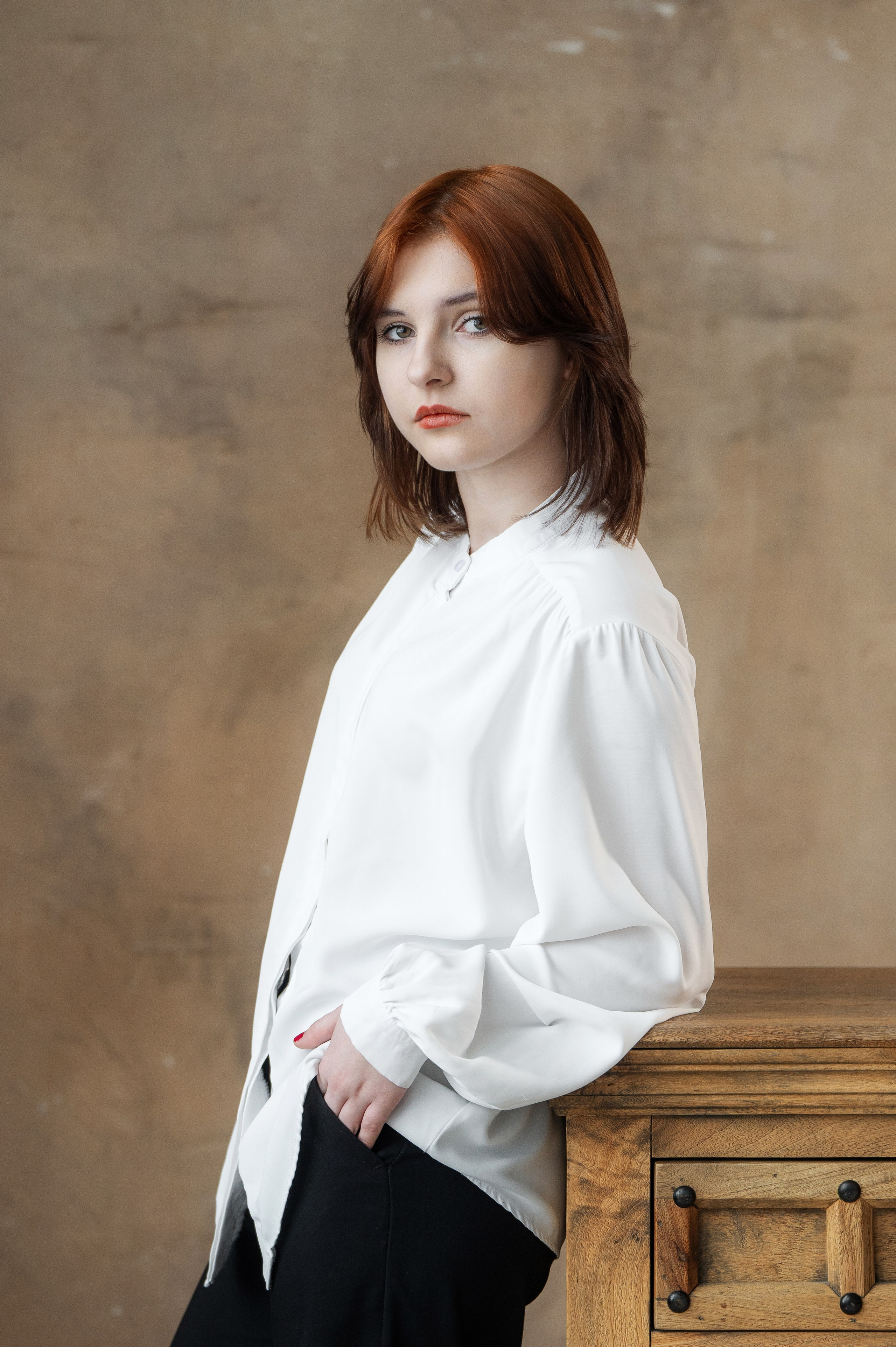 Портрет старшеклассницы в белой блузе у деревянной тумбы на тёплом фактурном фоне.