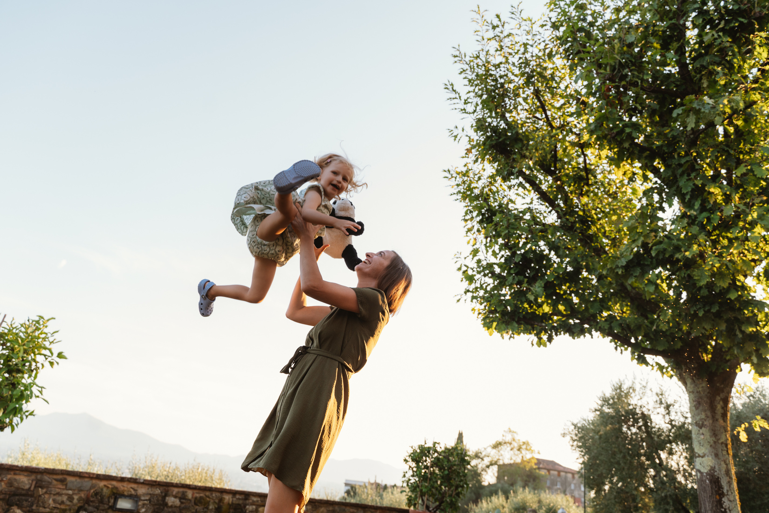 Parents and child playing together, silhouetted against the stunning colours of the setting sun in Tuscany.