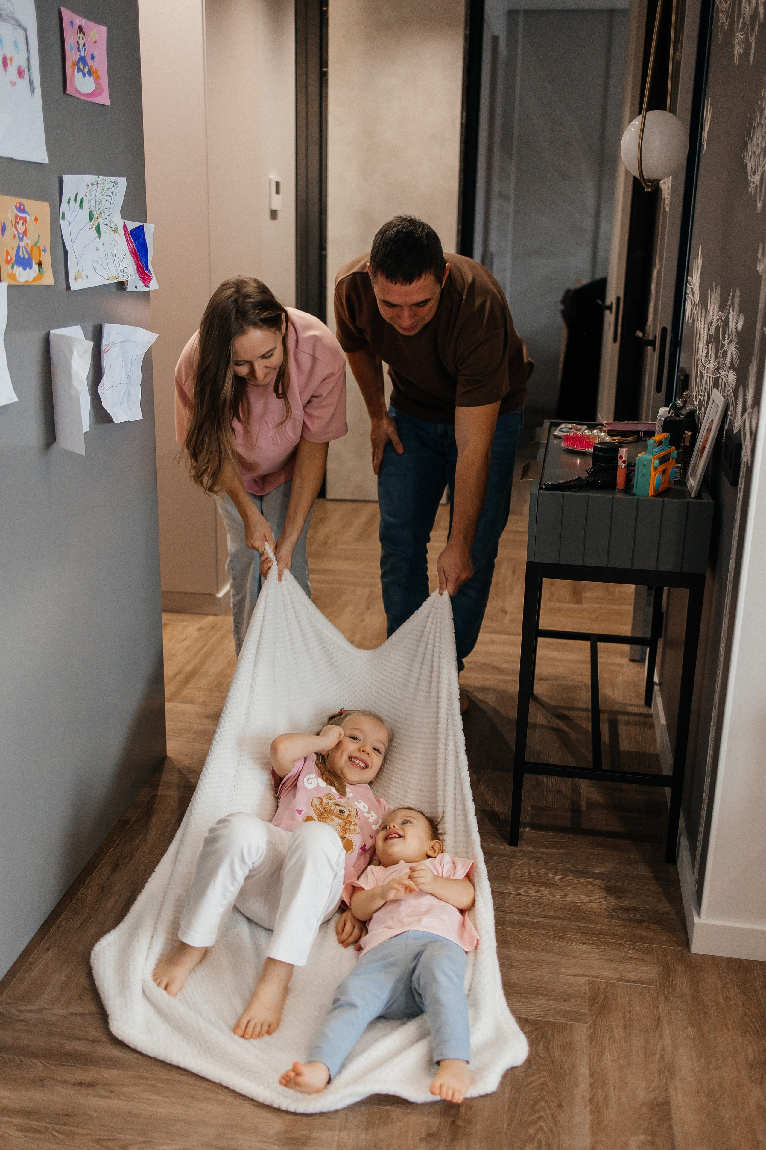 Естественная семейная съемка дома: родители щекочут детей 2 и 6 лет на родительской кровати