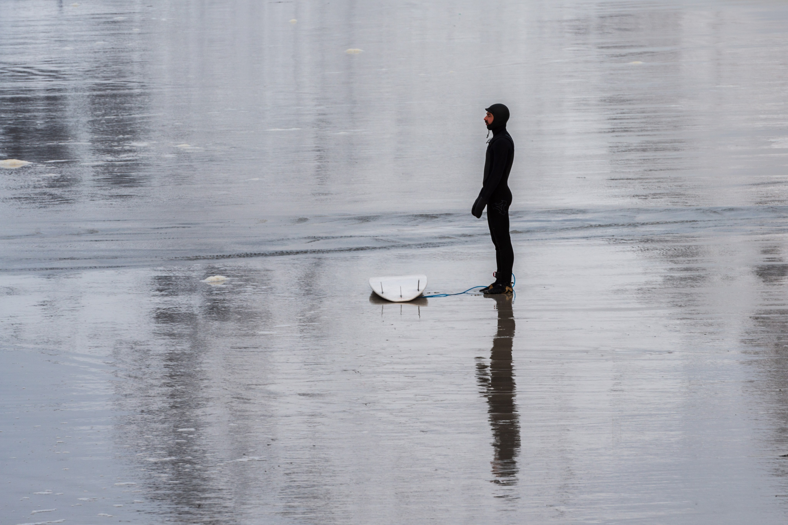 Surfer on the Arctic shore surrounded by snowy cliffs — экстремальный северный пейзаж Lofoten.