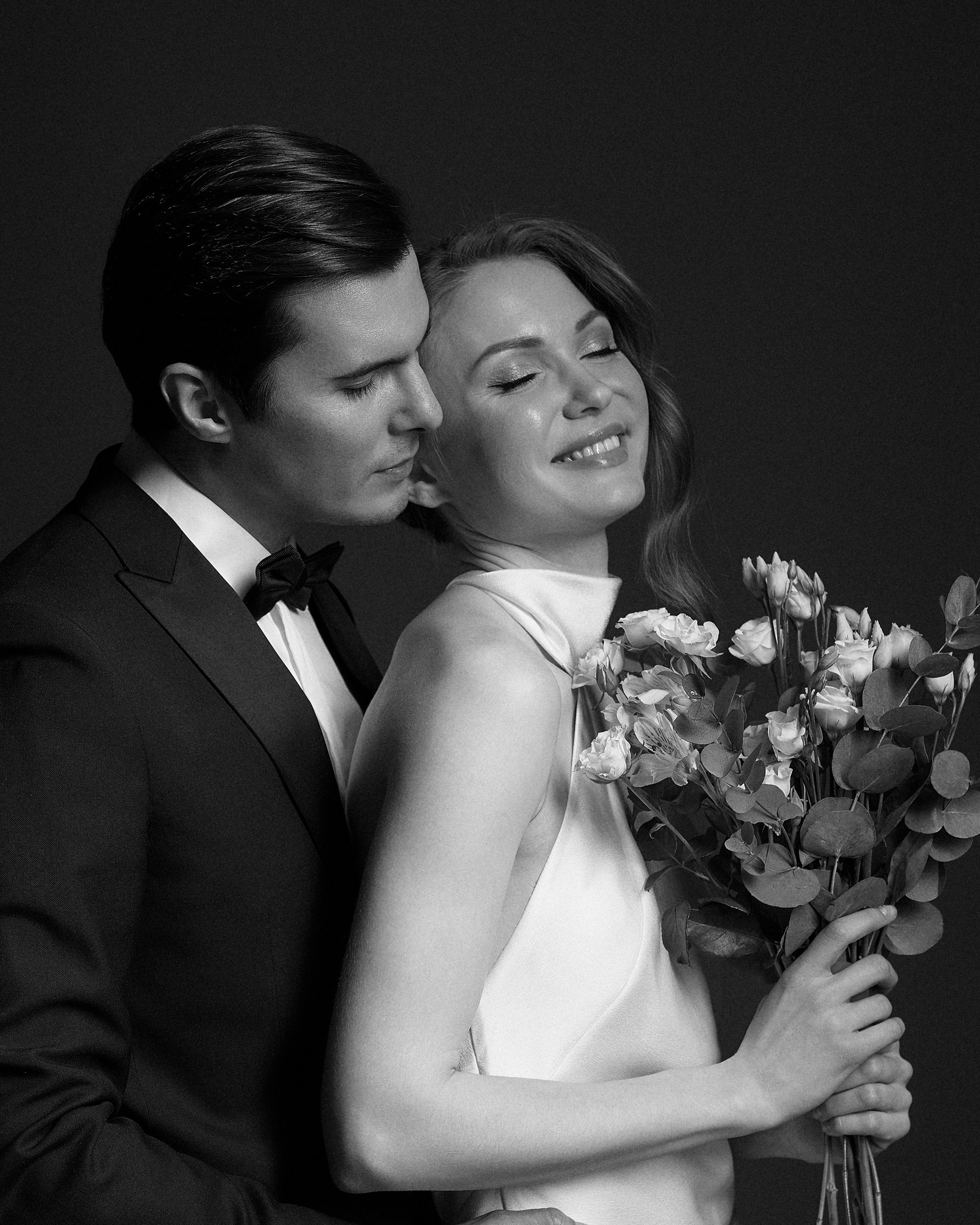 Жених обнимает невесту, их лица рядом, почти касаются. Тёмный фон подчёркивает каждый блик на коже и ткани. Очень чувственная и живая свадебная фотография. Фотограф Дмитрий Цветков, Санкт-Петербург