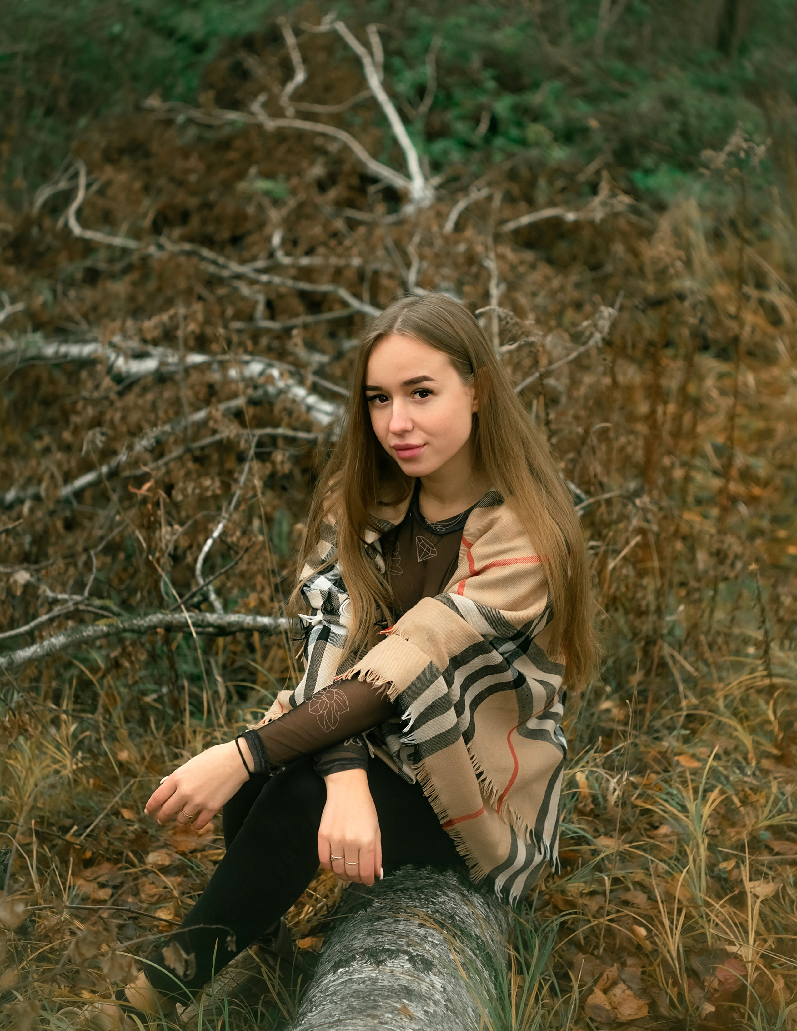 На фото девушка сидит на упавшем дереве.