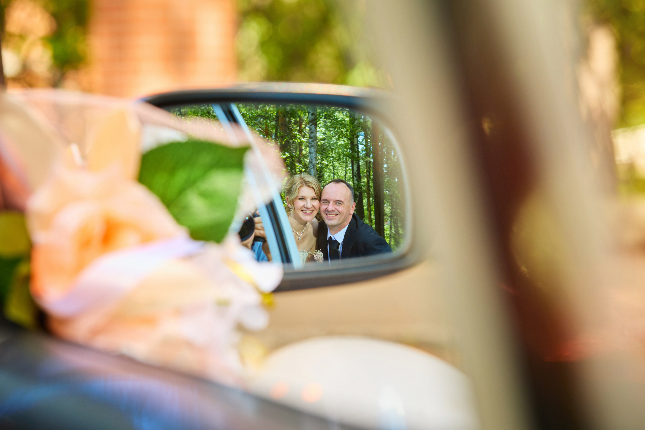 Жених и невеста в зеркале машины улыбаются