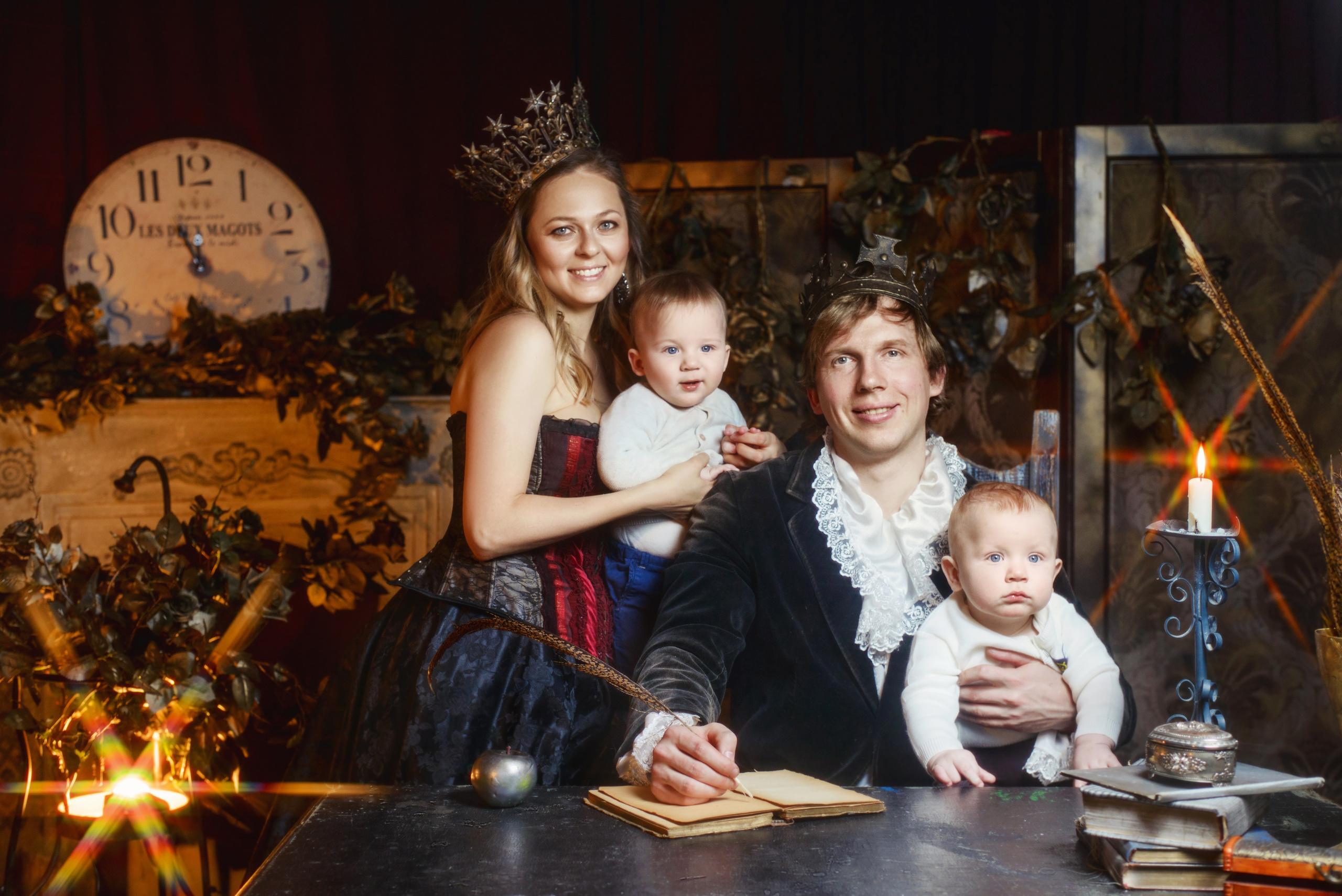 Мама и папа в костюме короля и королевы сидят за столом с маленькими сыновьями - близнецами