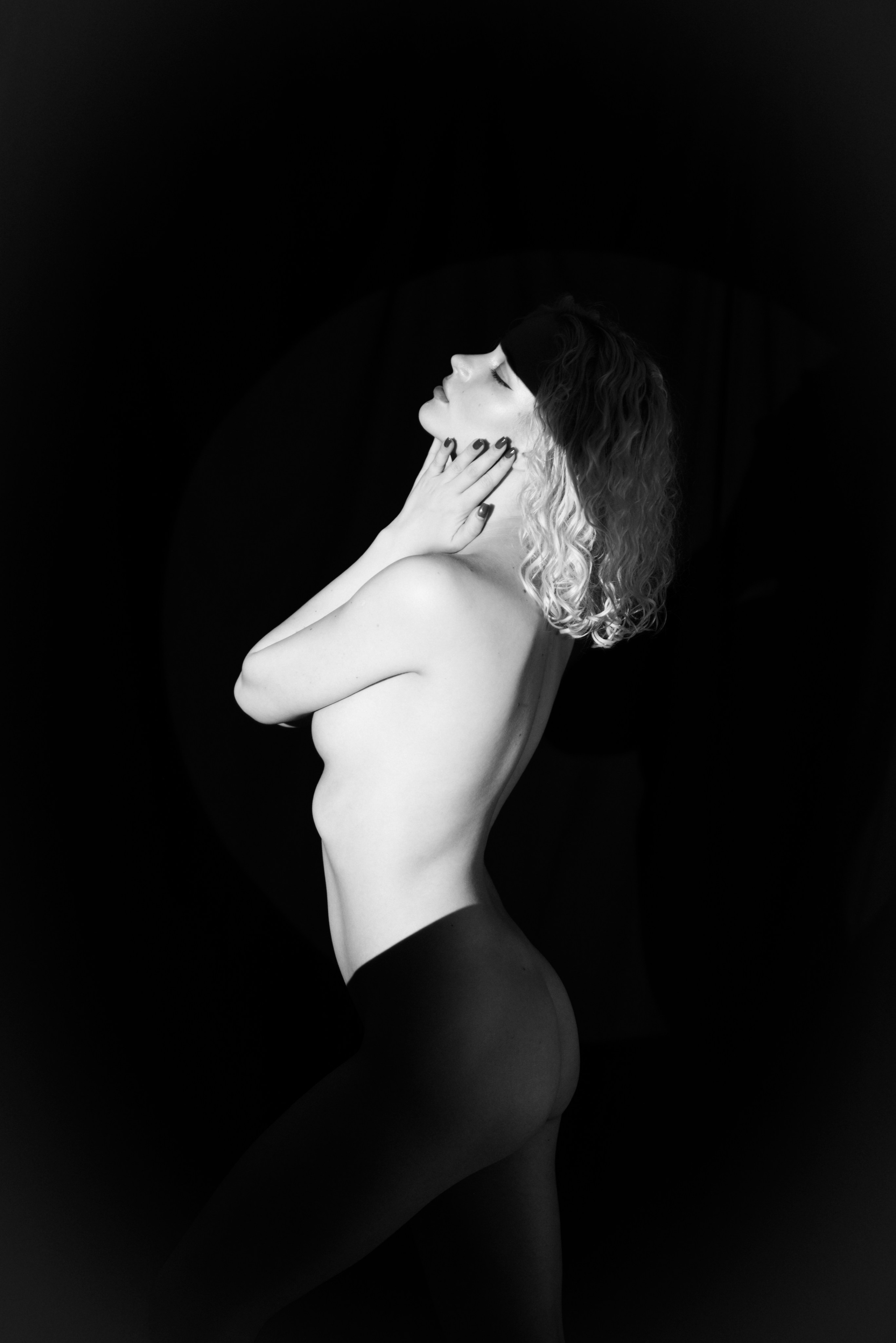 Boudoir London — dramatic black background portrait, woman with hand over mouth, artistic lighting, intimate style.
