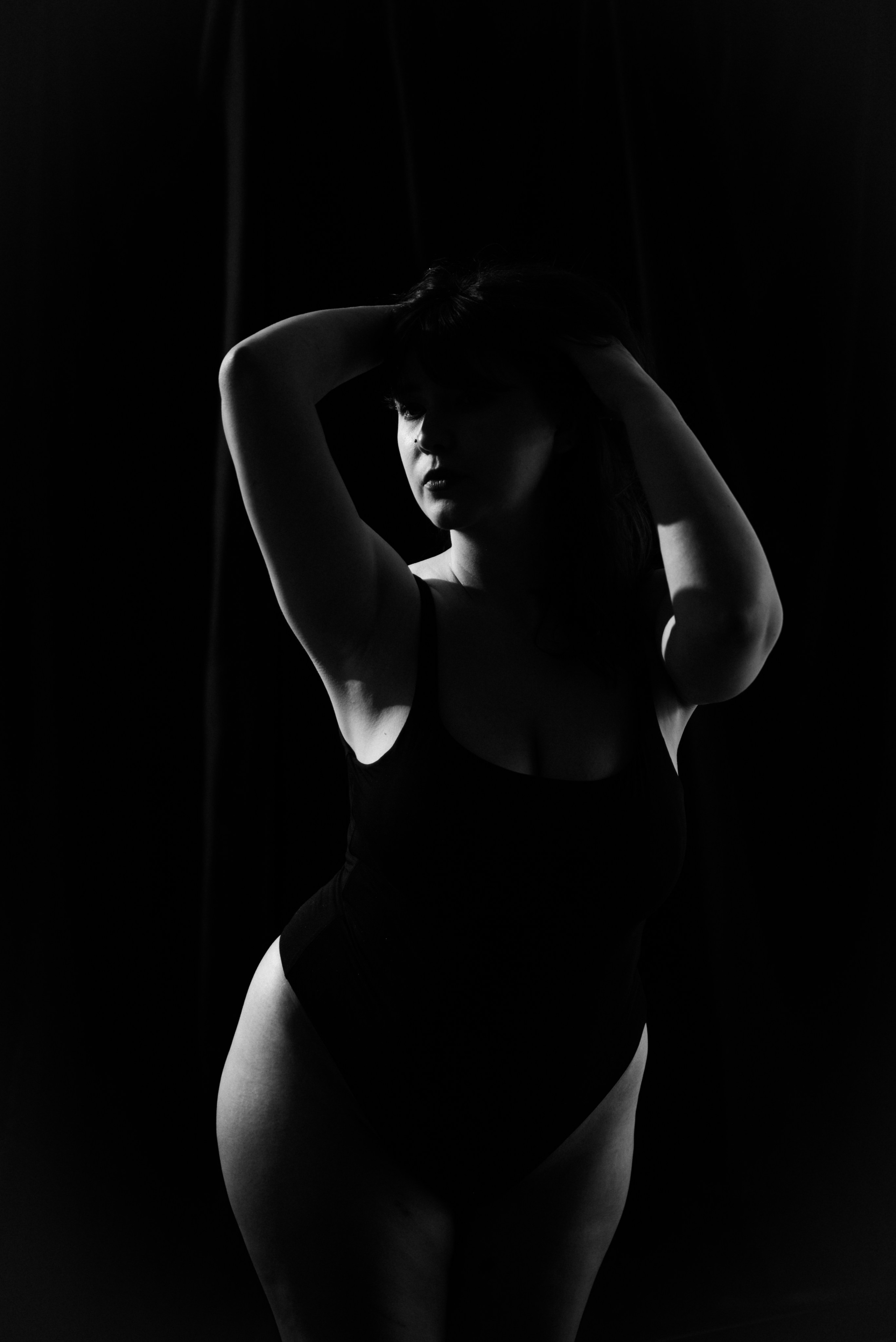Boudoir photoshoot London — strong silhouette of woman in black bodysuit, confident stance, dramatic lighting.