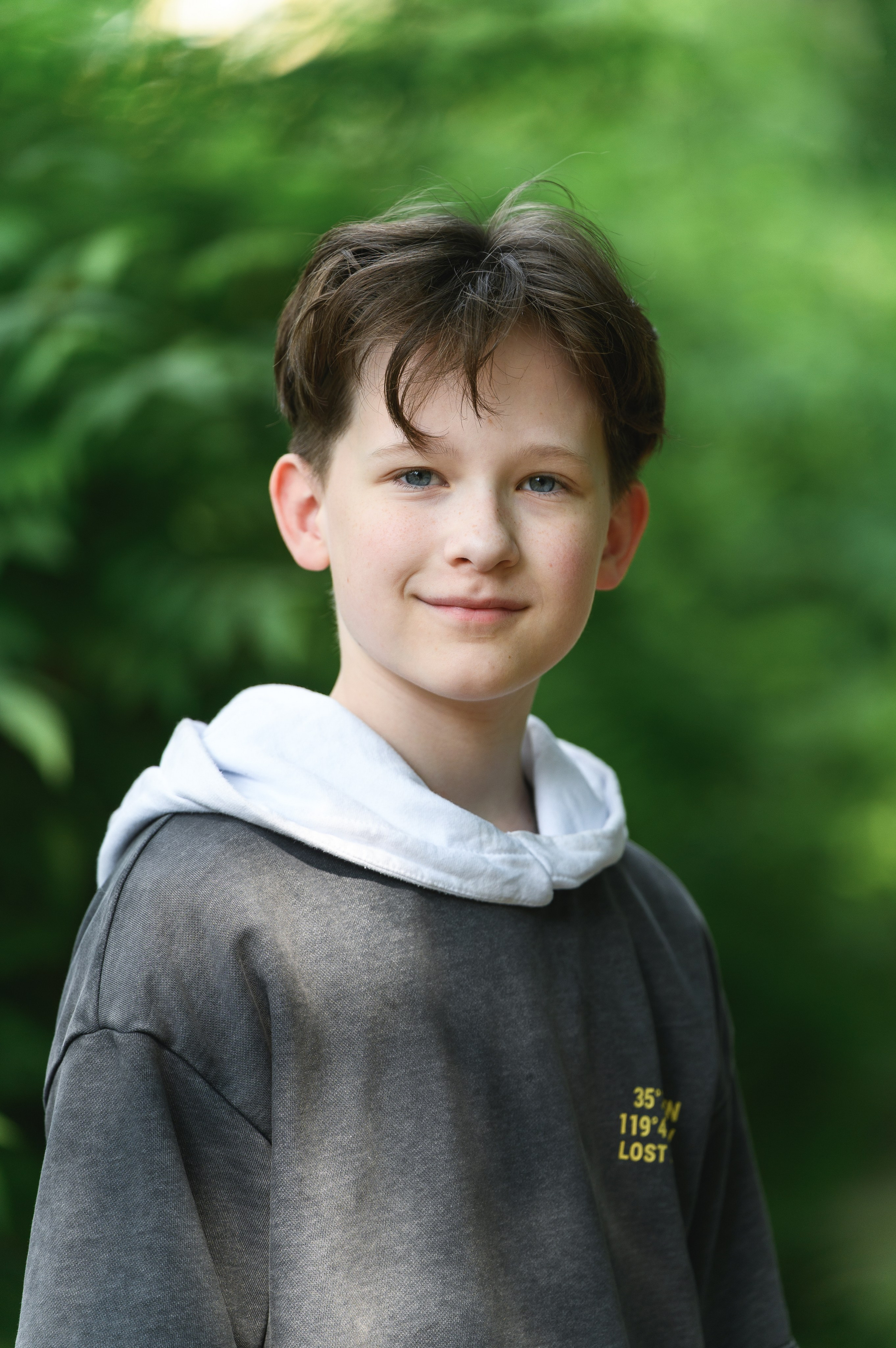 Портрет ученика в тёмном худи на размытом зелёном фоне