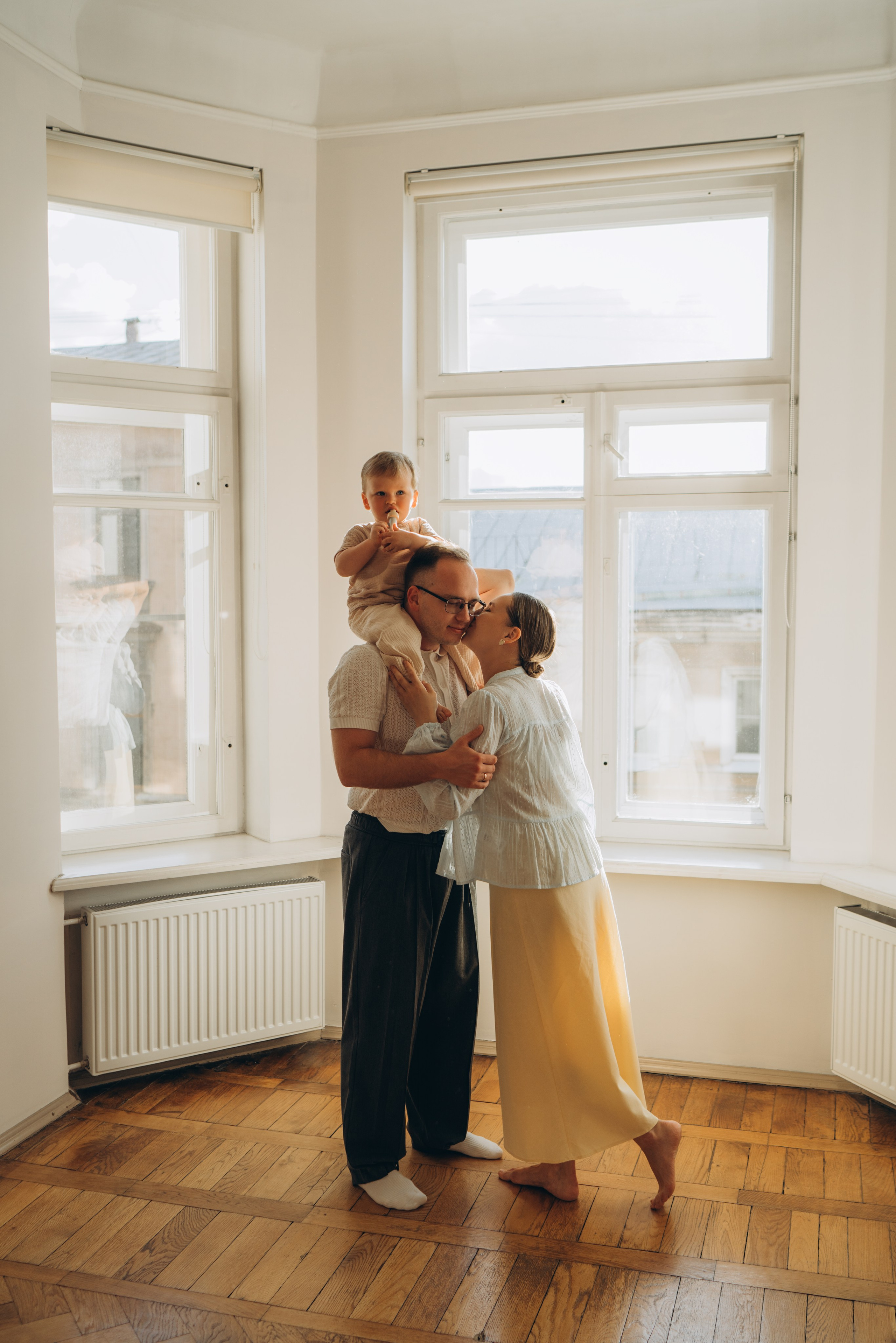 Родители обнимаются с ребёнком у окна во время семейной фотосессии
