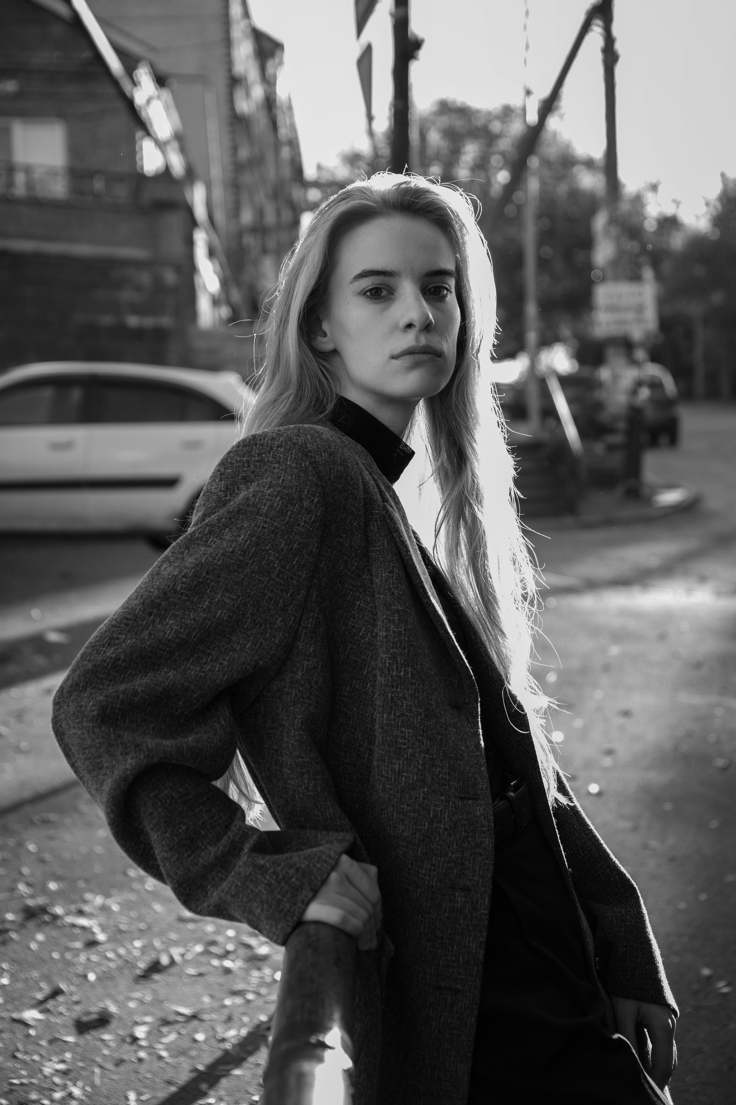 Черно-белая фотография девушки с длинными светлыми волосами в замшевом пиджаке на улице в контровом солнечном свете