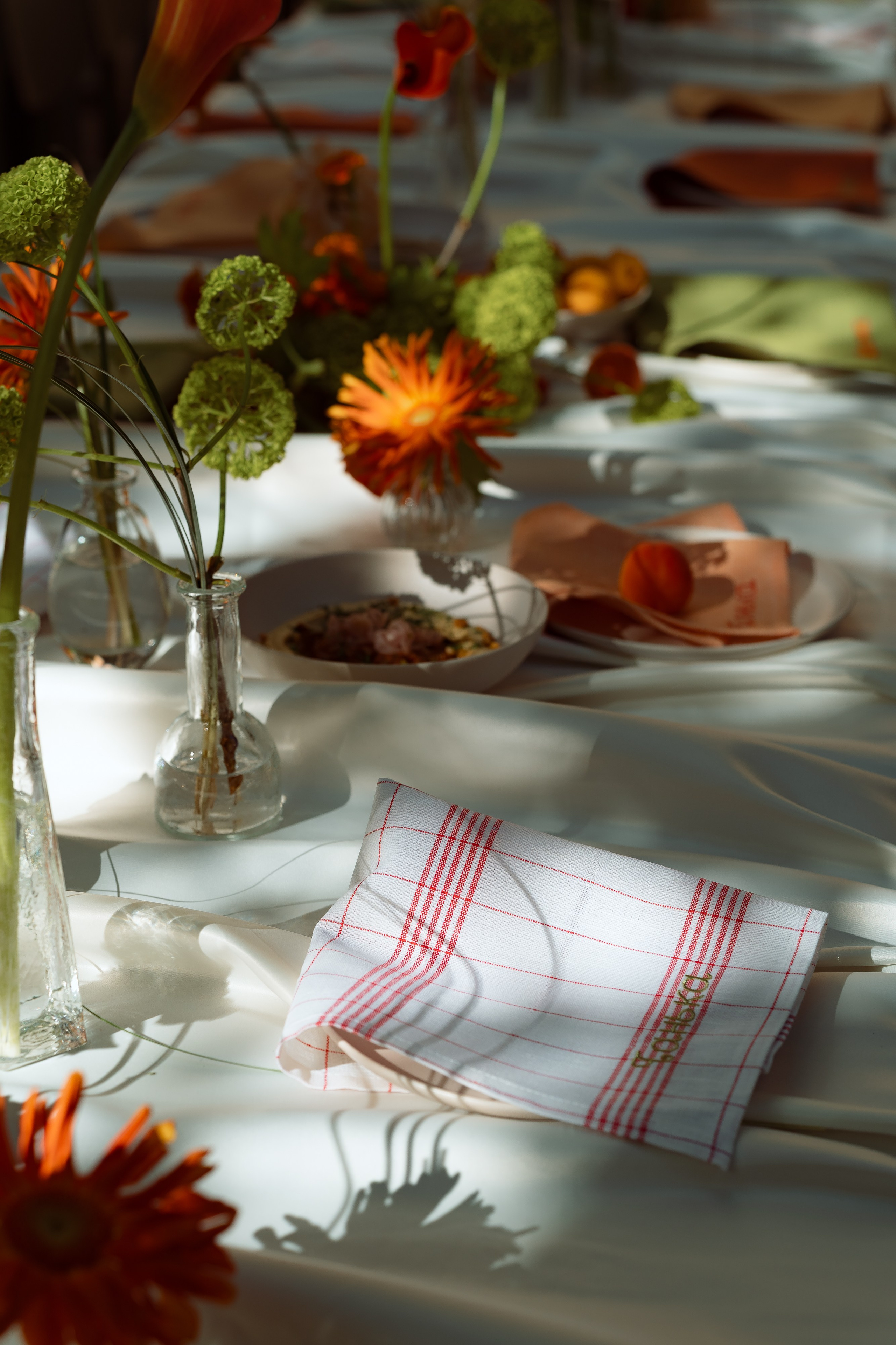Сервировка: белые тарелки, льняные салфетки и георгины, блики солнца на скатерти