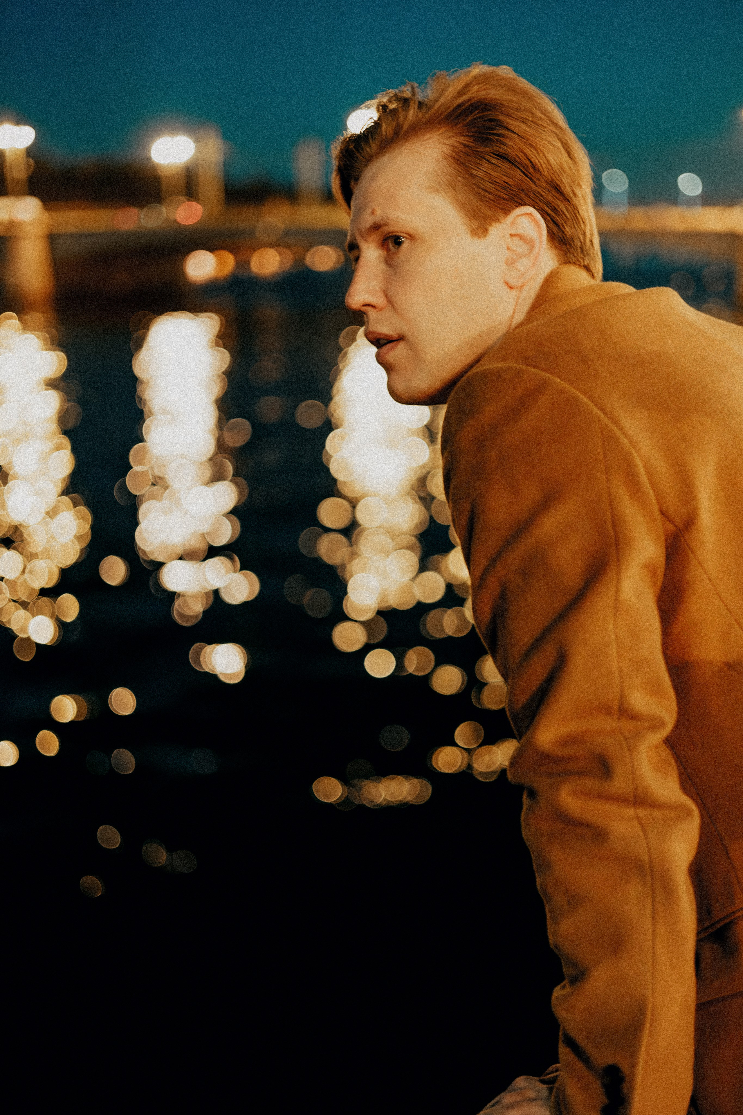 Молодой человек в пальто перелезает через перила на набережной.