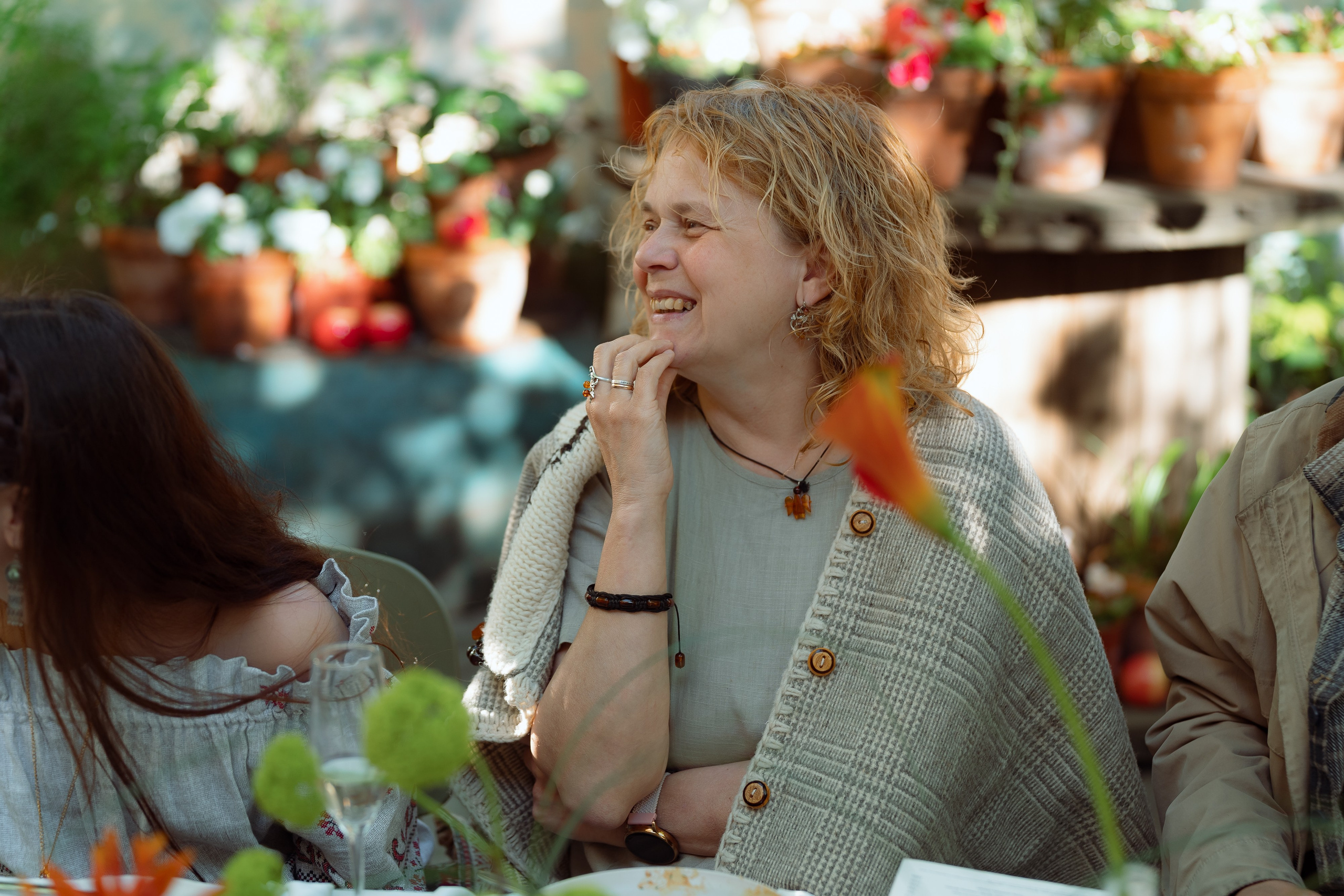 Кудрявая гостья слушает тост, вокруг глиняные горшки с цветами