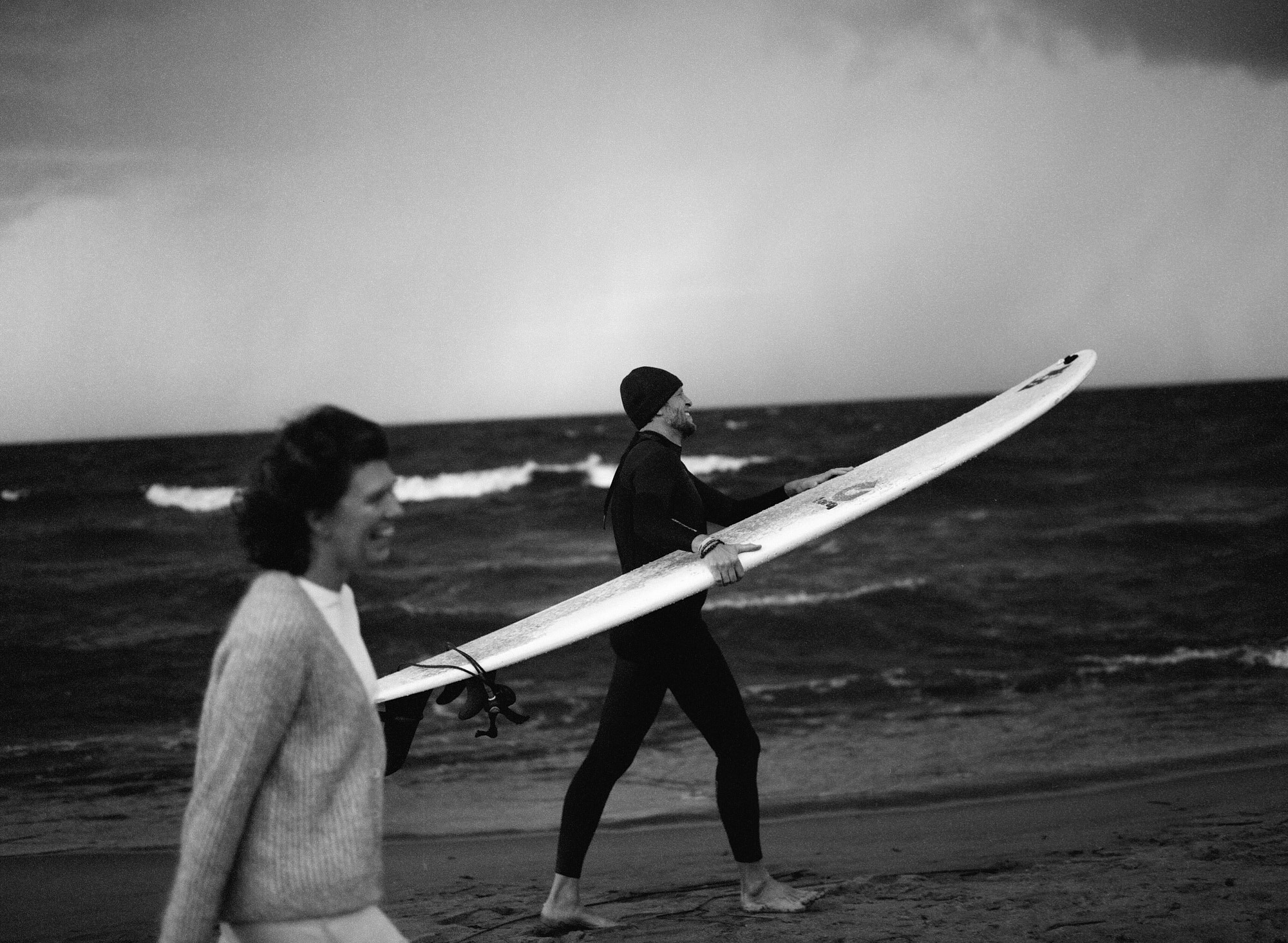 Чёрно-белый плёночный кадр: пара с сёрфбордом на берегу Финского залива