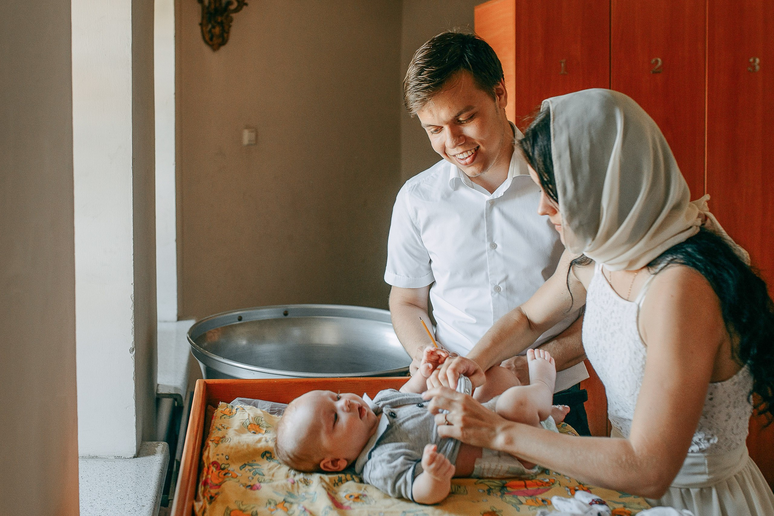 Фотограф на крещение в Новосибирске: родители переодевают младенца перед началом таинства в храме.