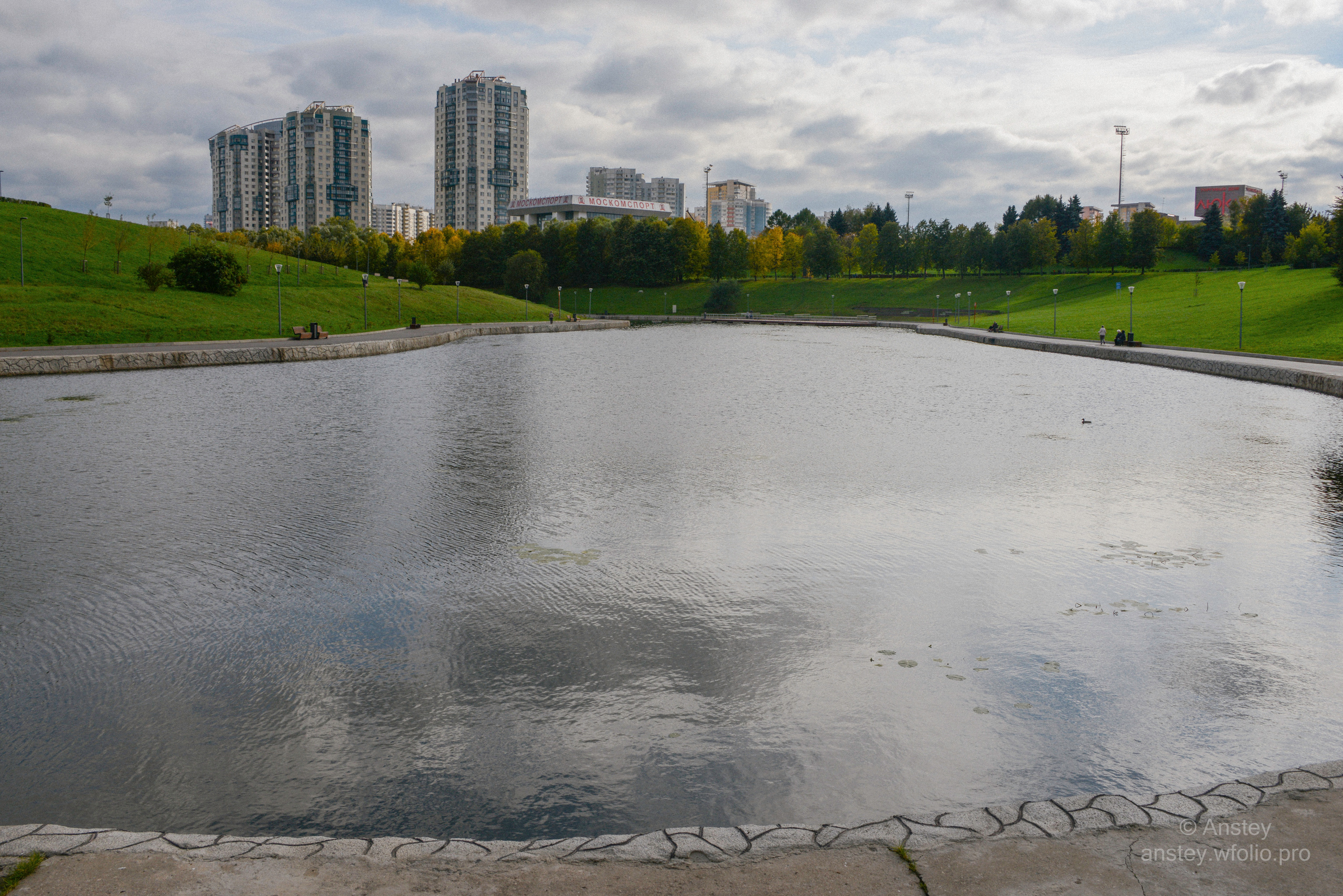 Scenic view in a city park, pond and sky in early autumn season.