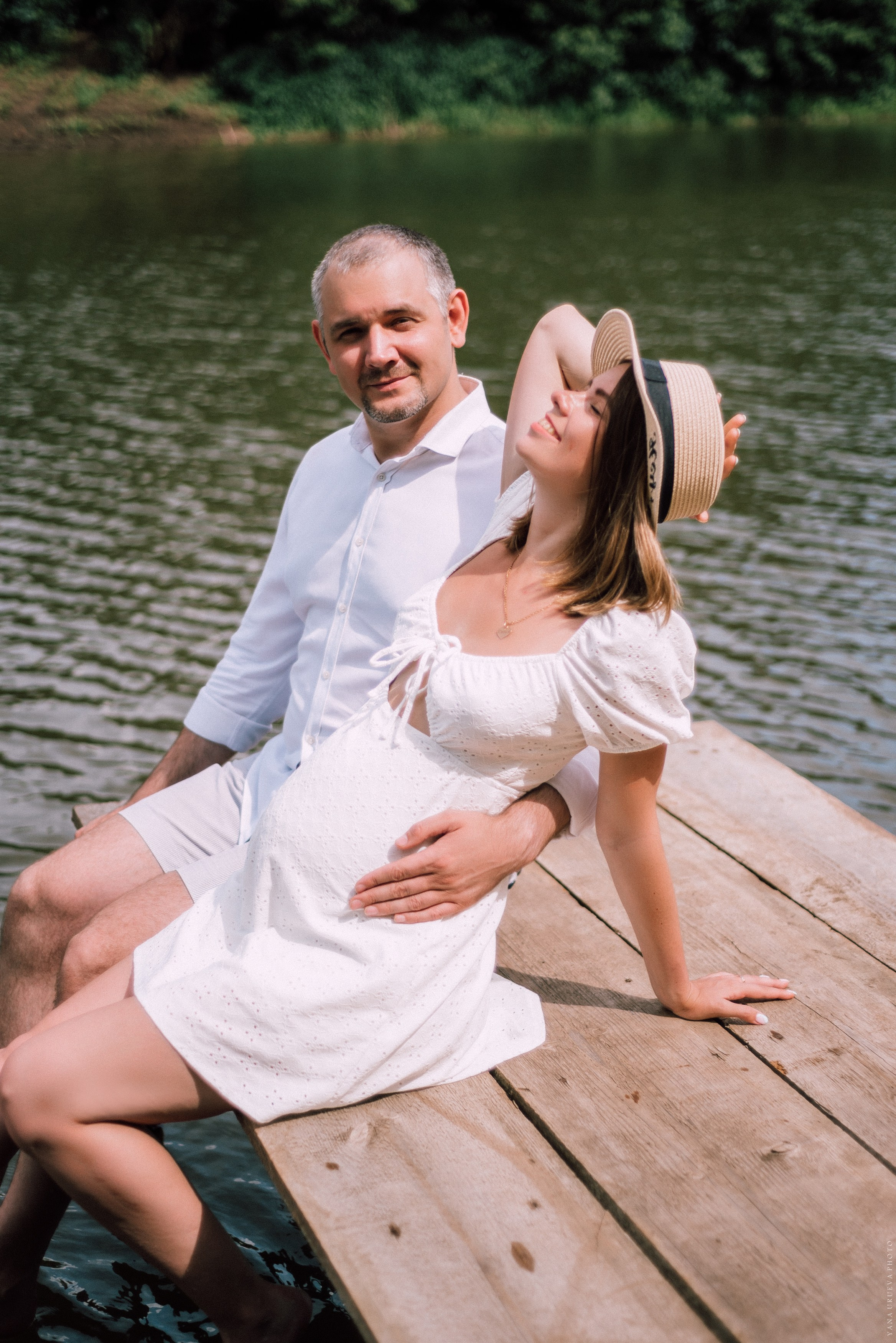 Беременная девушка сидит на пирсе у реки