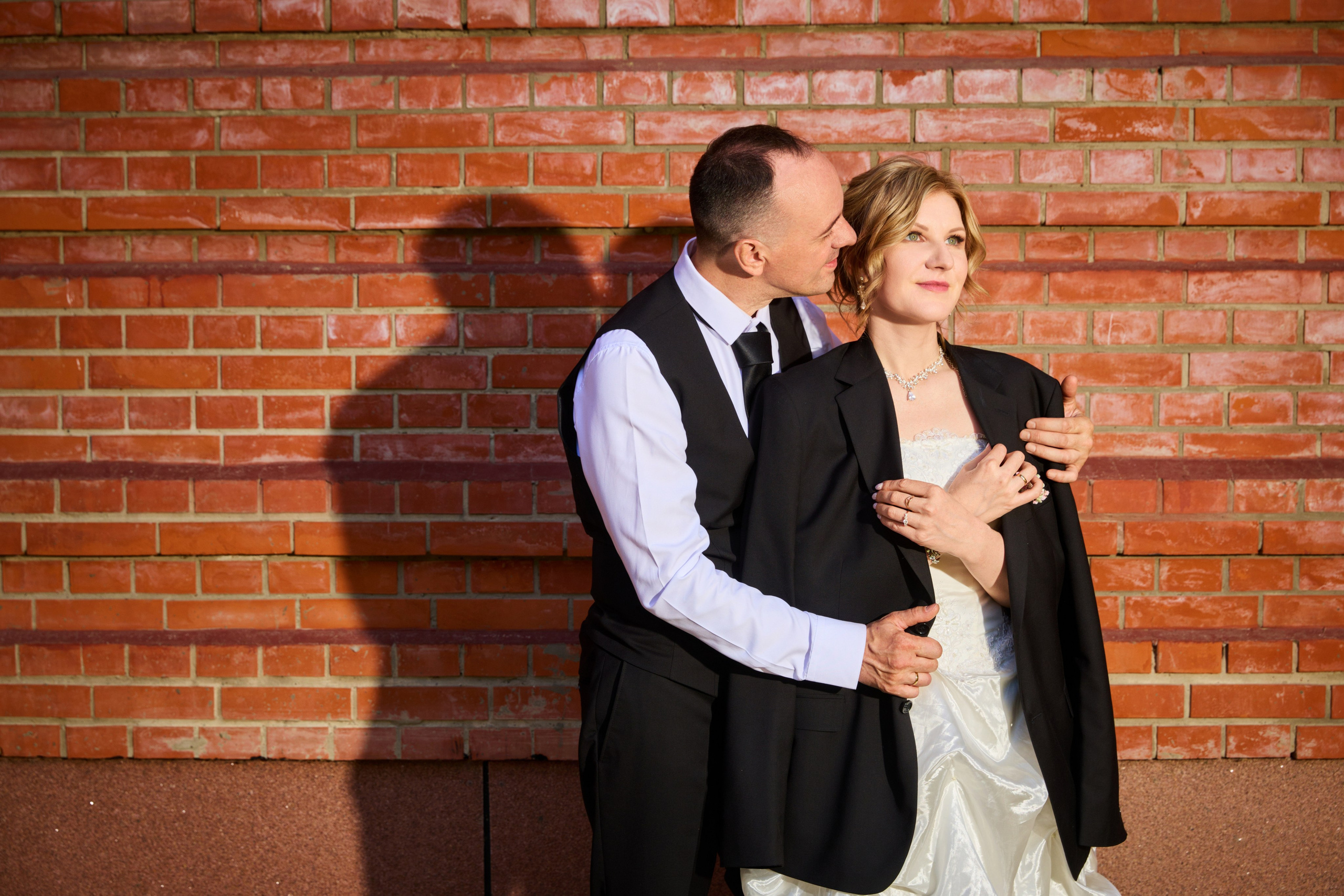 На фоне кирпичной стены жених накинул пиджак на невесту