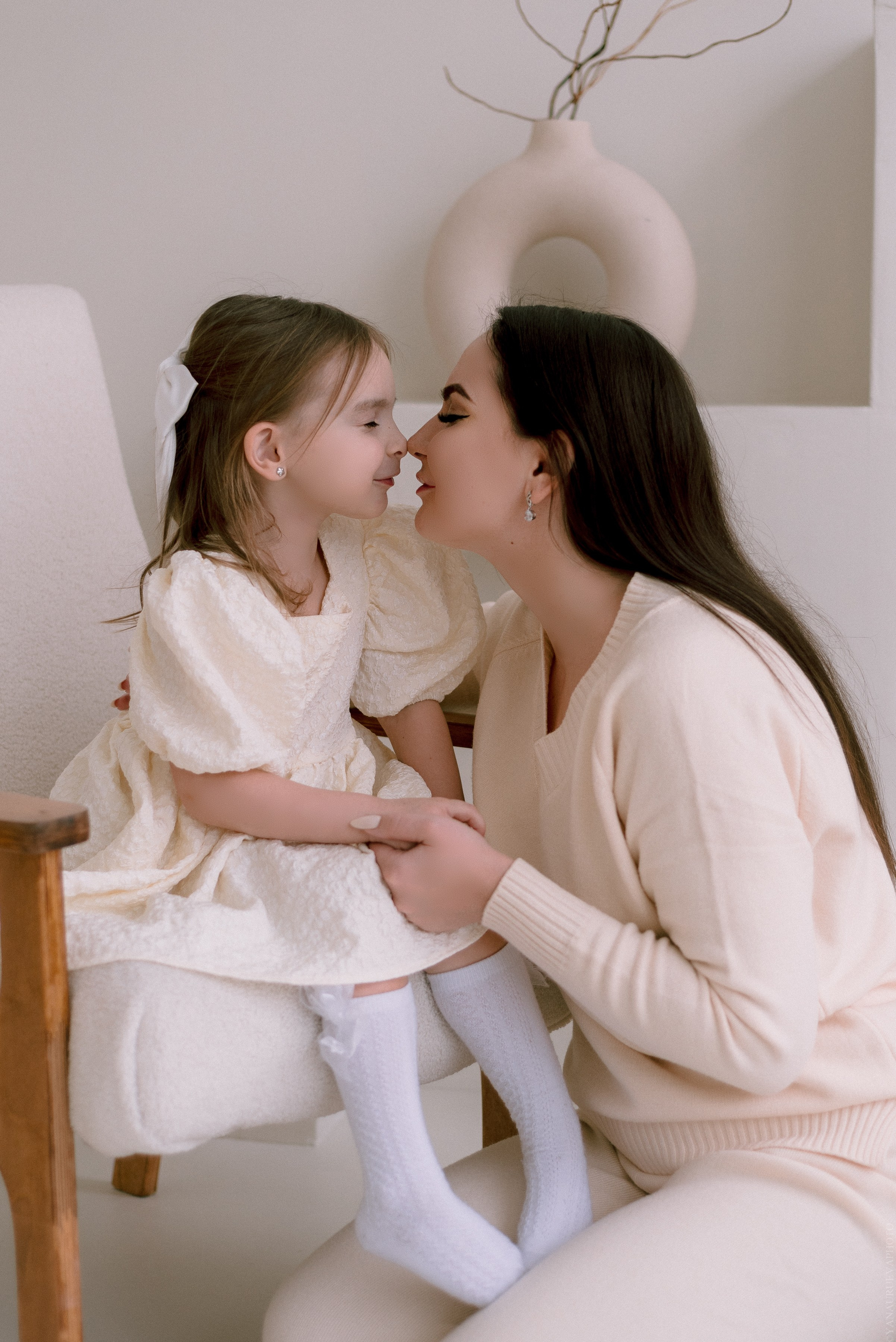 Мама целует дочку в носик, в бежевых тонах