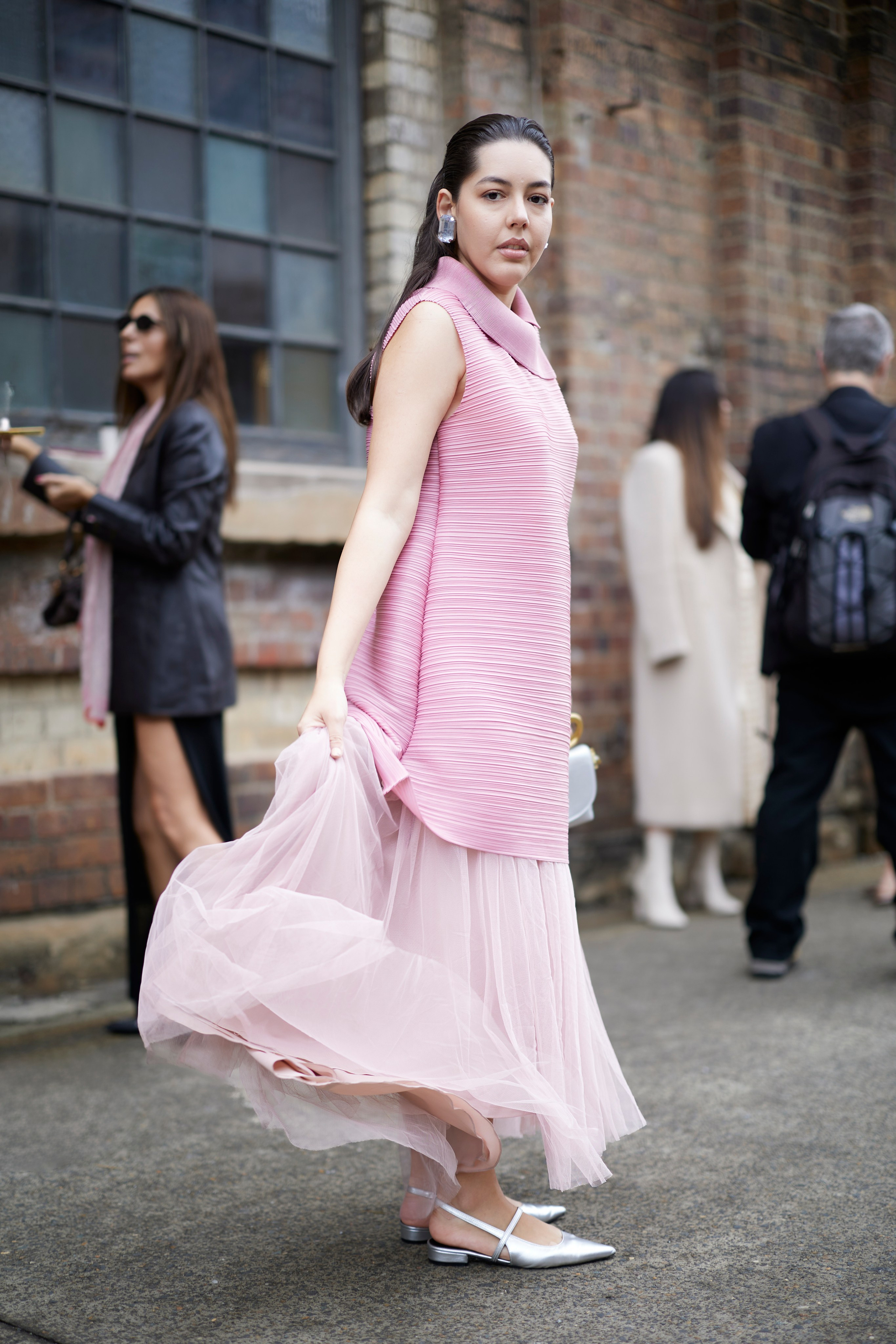 Stylist Valeria Bush wears a flowing pastel pink outfit with a pleated top and sheer tulle skirt, complemented by metallic flats, outside Carriageworks during Australian Fashion Week 2025. Photographed by Maria Poleshchuk.