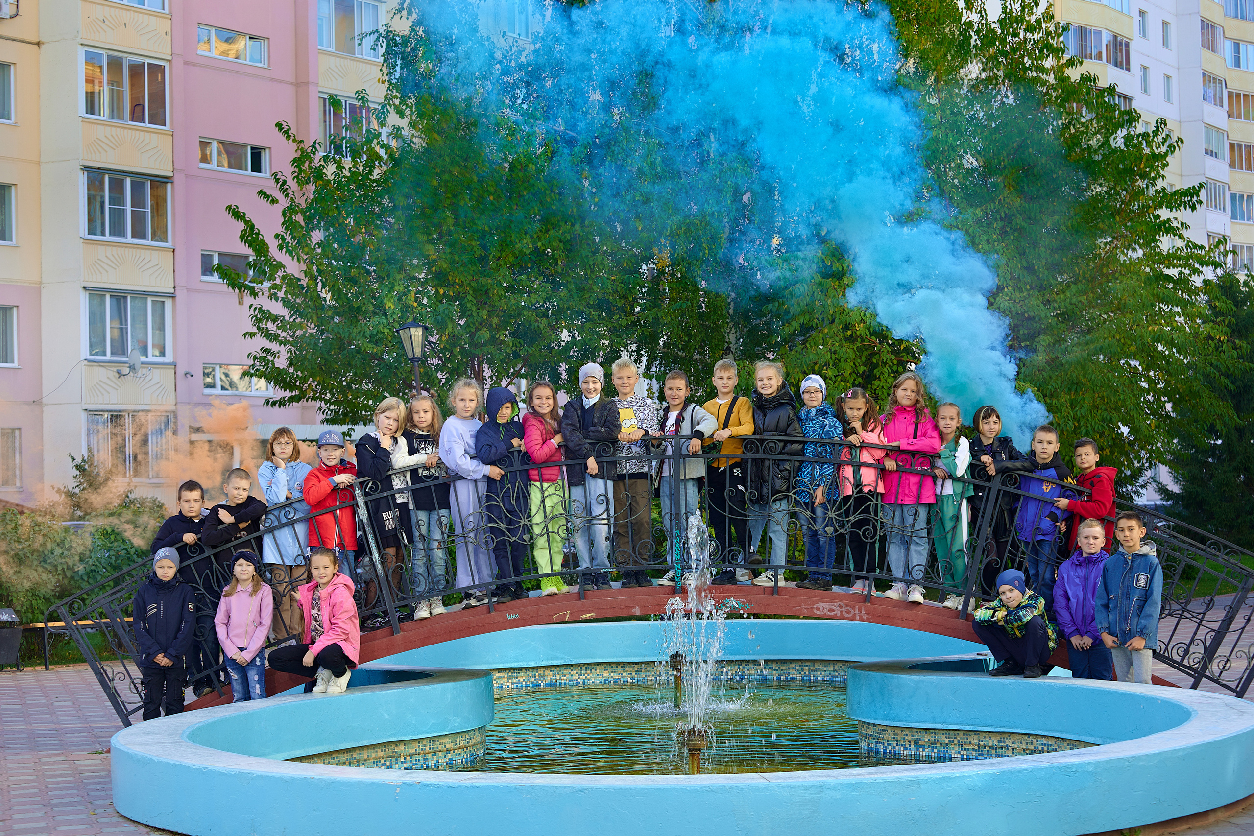 Дети, ученики четвертого класса фотографируются у фонтана, держат в руках дымовую шашку синего цвета.