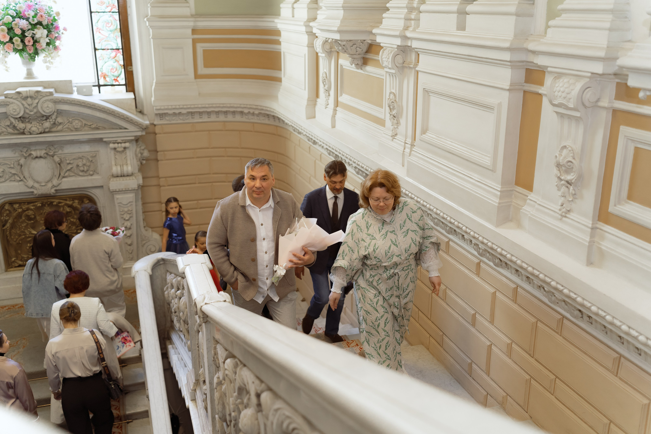 Гости и молодожёны поднимаются по парадной лестнице в ЗАГСе