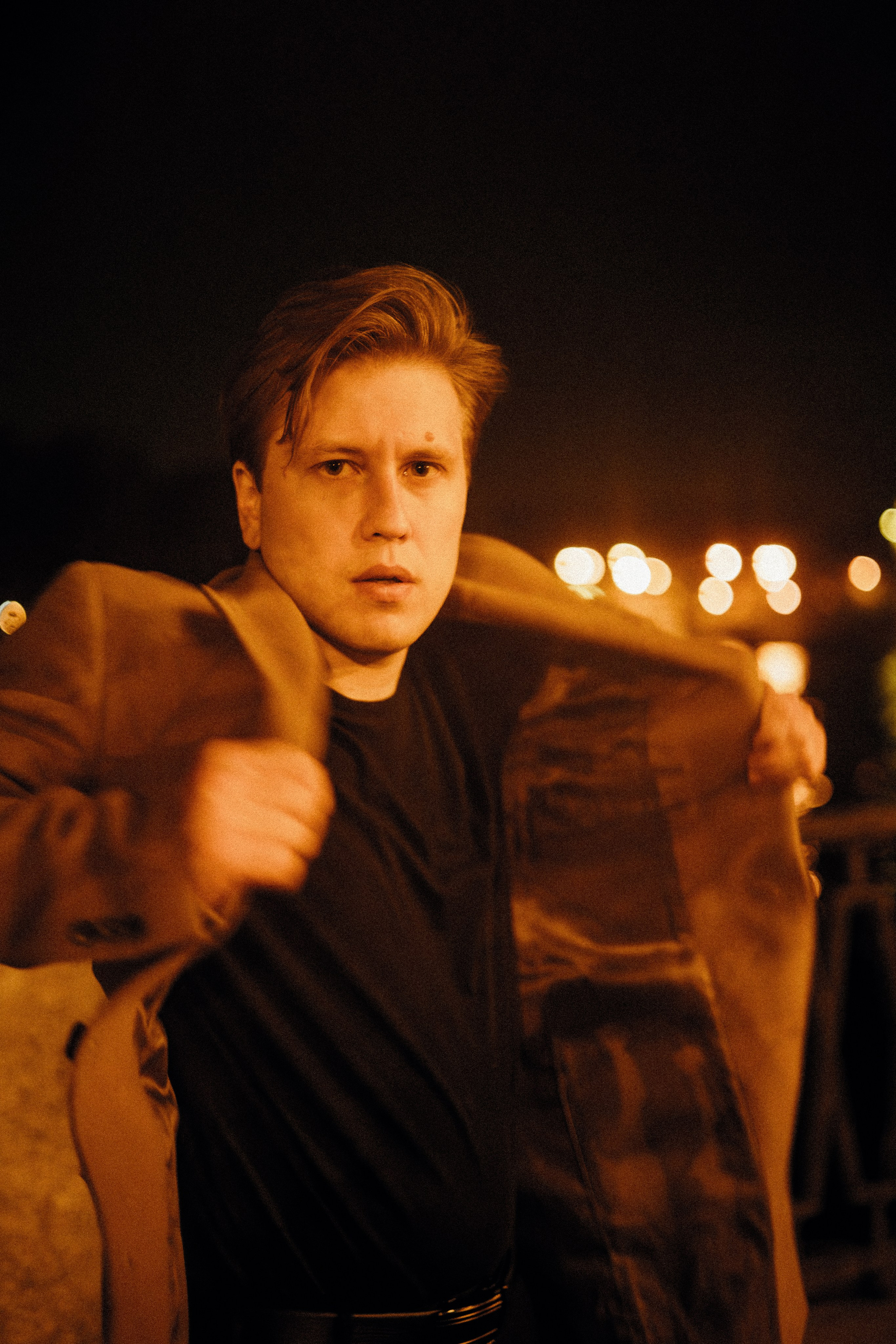 Молодой человек в пальто смотрит в камеру на набережной.