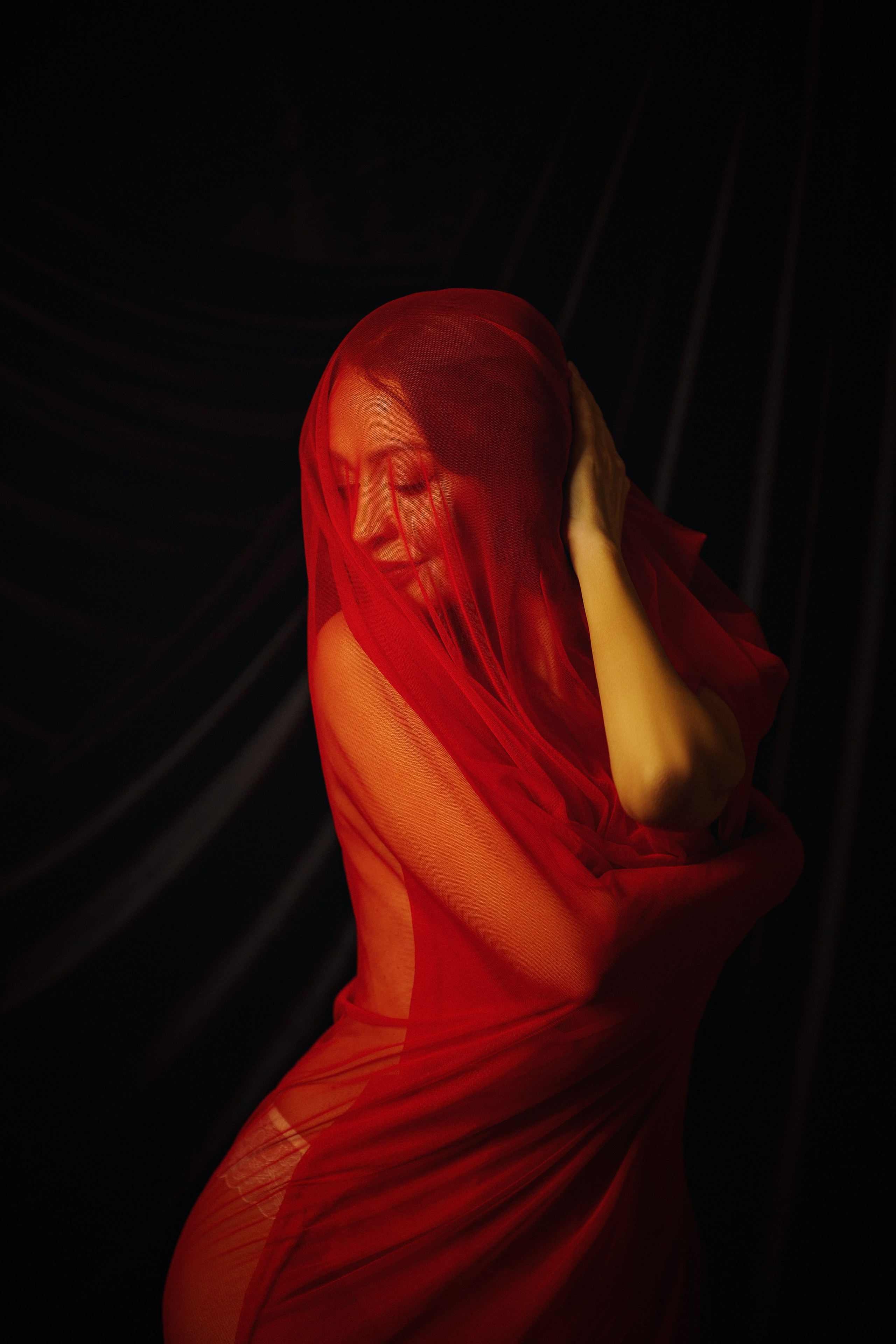 Художественная ню фотография, на которой женщина, накрытая красной тканью при студийном свете