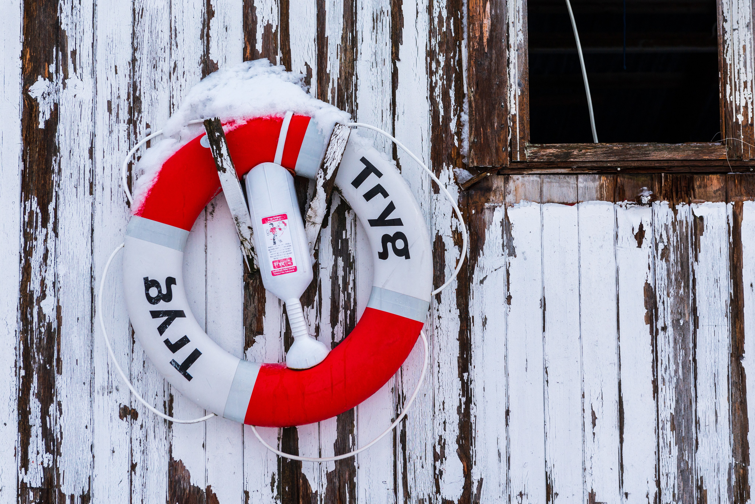 Красно-белый спасательный круг «Tryg» висит на стене из состаренных деревянных досок.