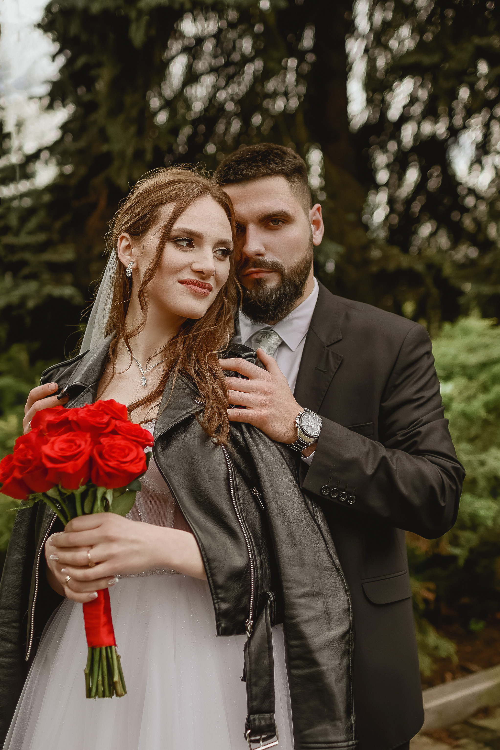 Жених и невеста в черных пиджаках с букетом красных роз