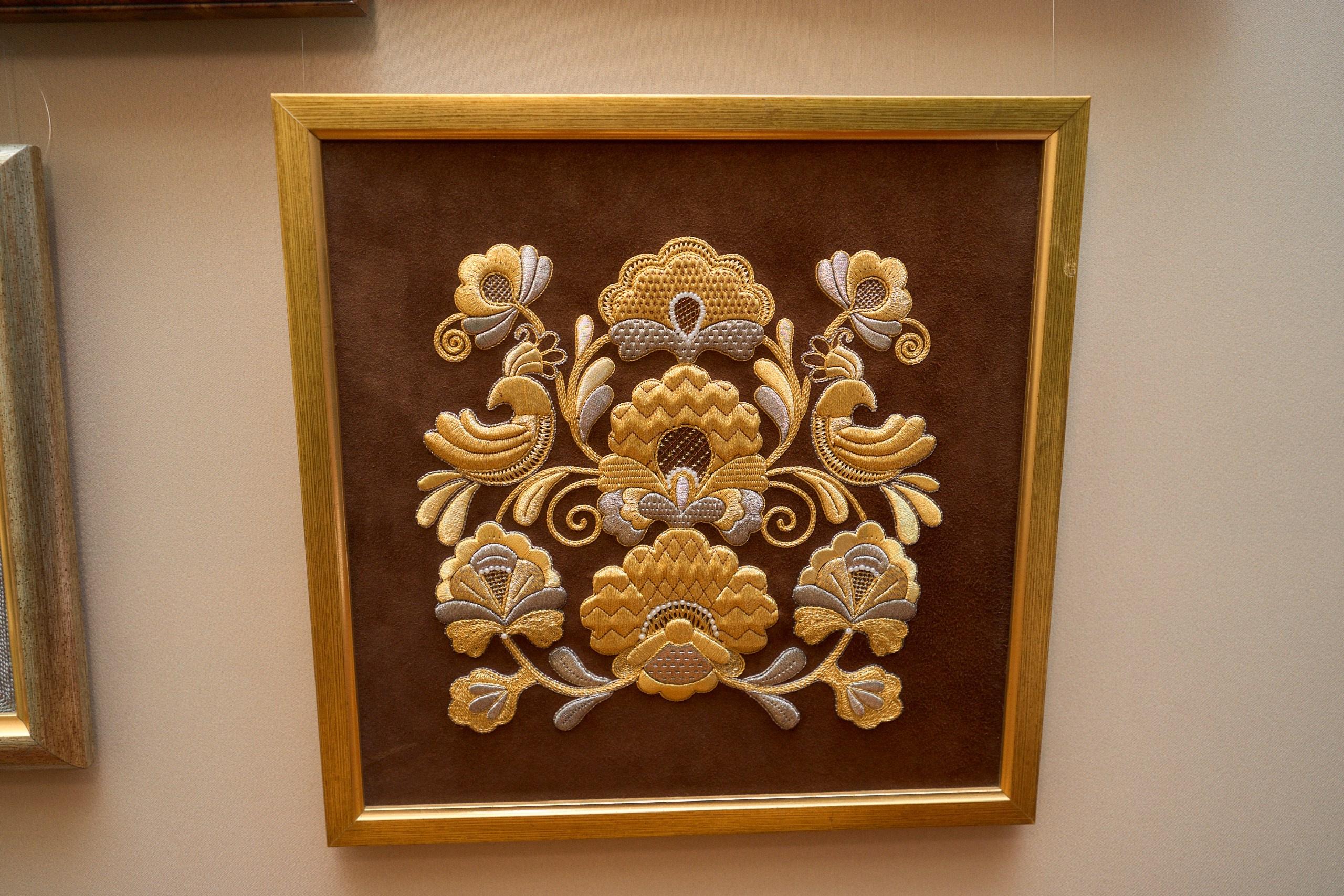 Традиционная торжокская золотошвейная вышивка в раме, демонстрируемая в Музее торжокских золотошвей в Торжке. Вышивка выполнена на тёмном фоне с использованием золотых и серебряных нитей, создающих сложный орнамент с элементами растительных мотивов и стилизованных птиц.