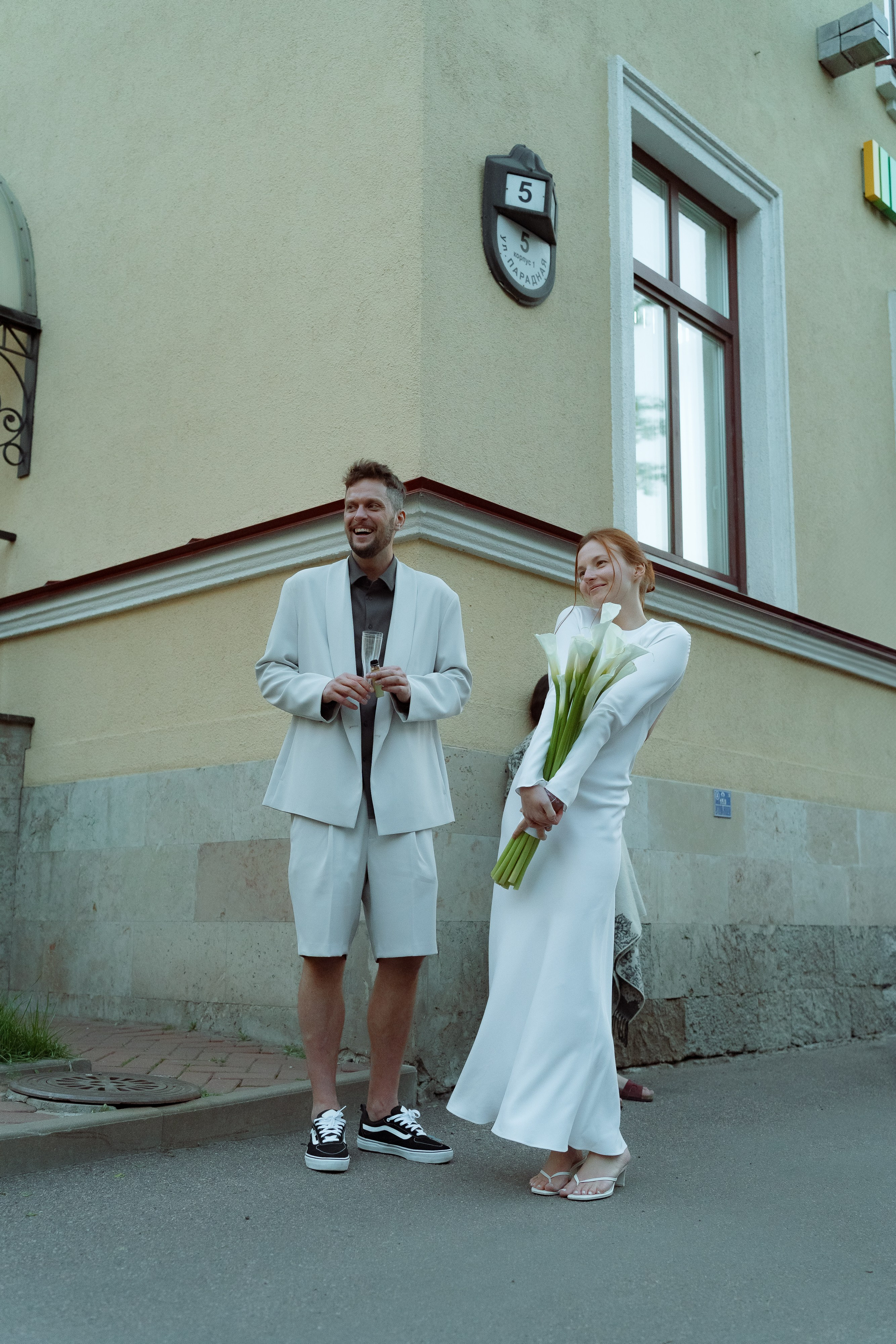 Пара позирует у угла старинного здания, невеста держит белые каллы