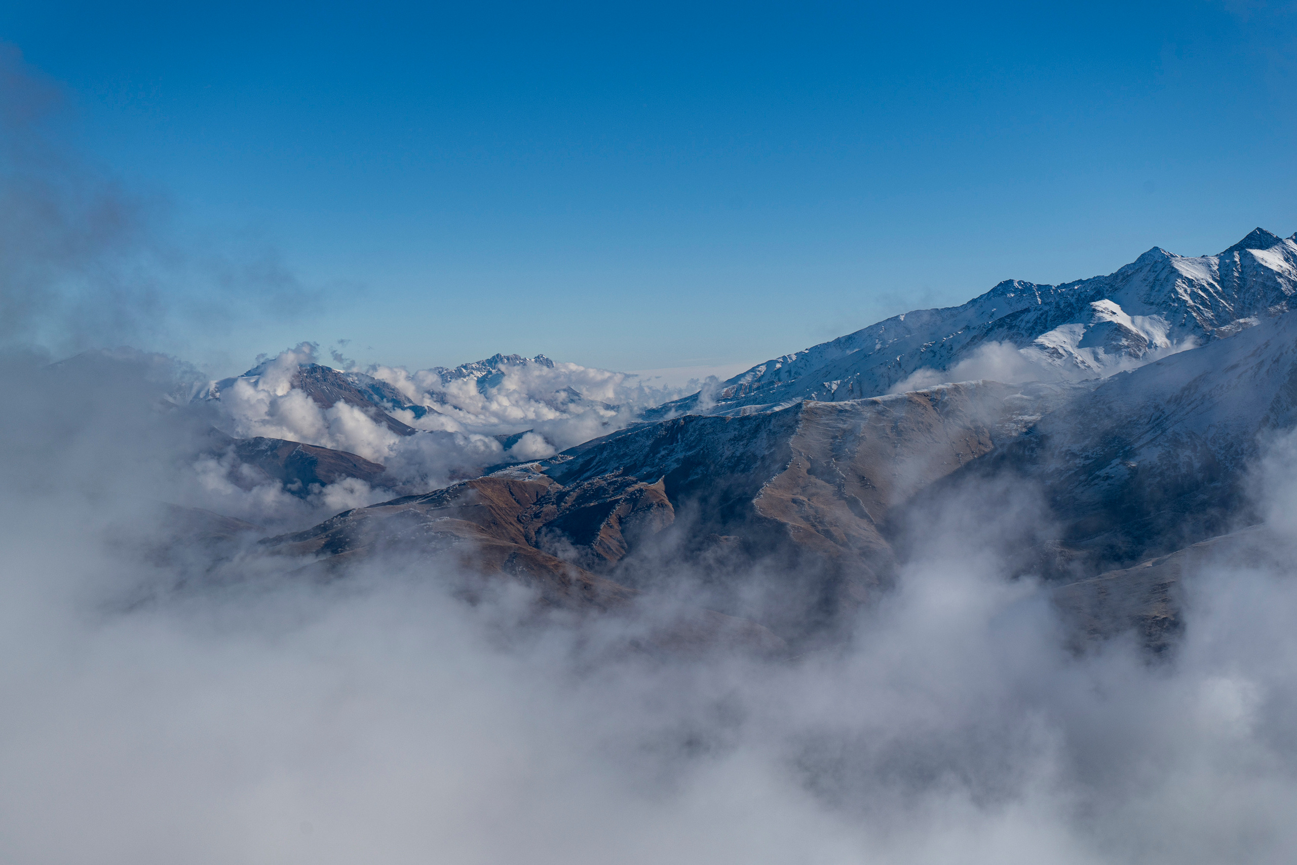 Вид с высоты 2500 метров над уровнем моря. Заснеженные вершины гор в облаках. Такой пейзаж открывается с площадке, на которой находится лавочка счастья
